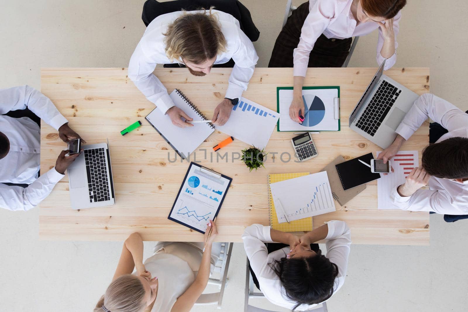 Business people brainstorming at office desk analyzing financial reports and pointing out financial data on a sheet, top view