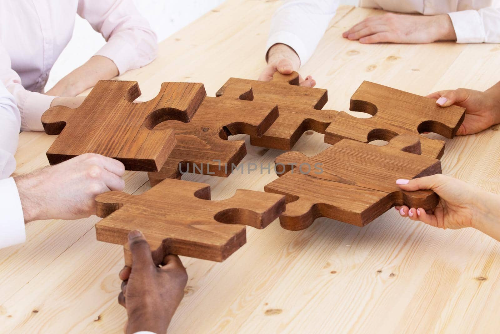 Business people team sitting around meeting table and assembling wooden jigsaw puzzle pieces unity cooperation ideas concept