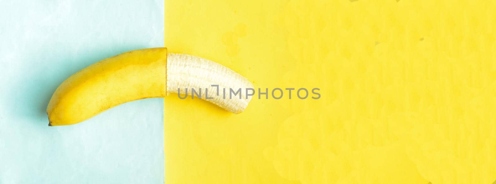 One partially peeled banana on blue yellow background, cpyspace.Tropic summer fruit