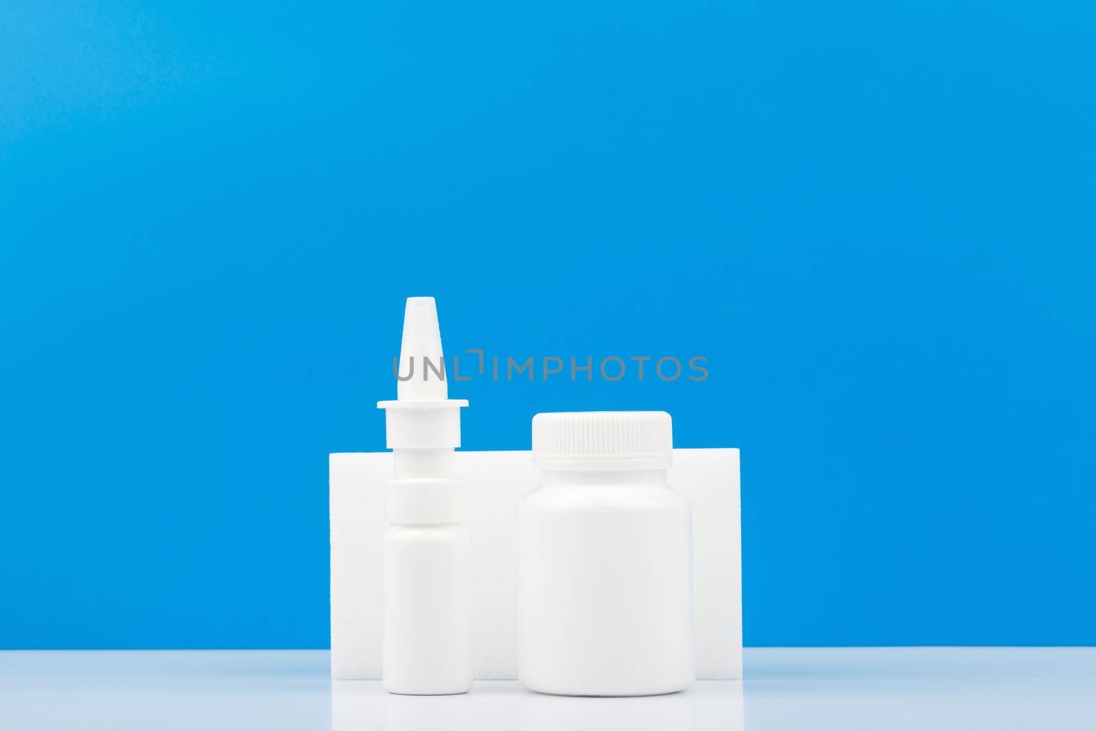 Nose spray and medication bottle on white table against blue background with copy space. Concept of pharmacy and medication treatment during flu and running nose
