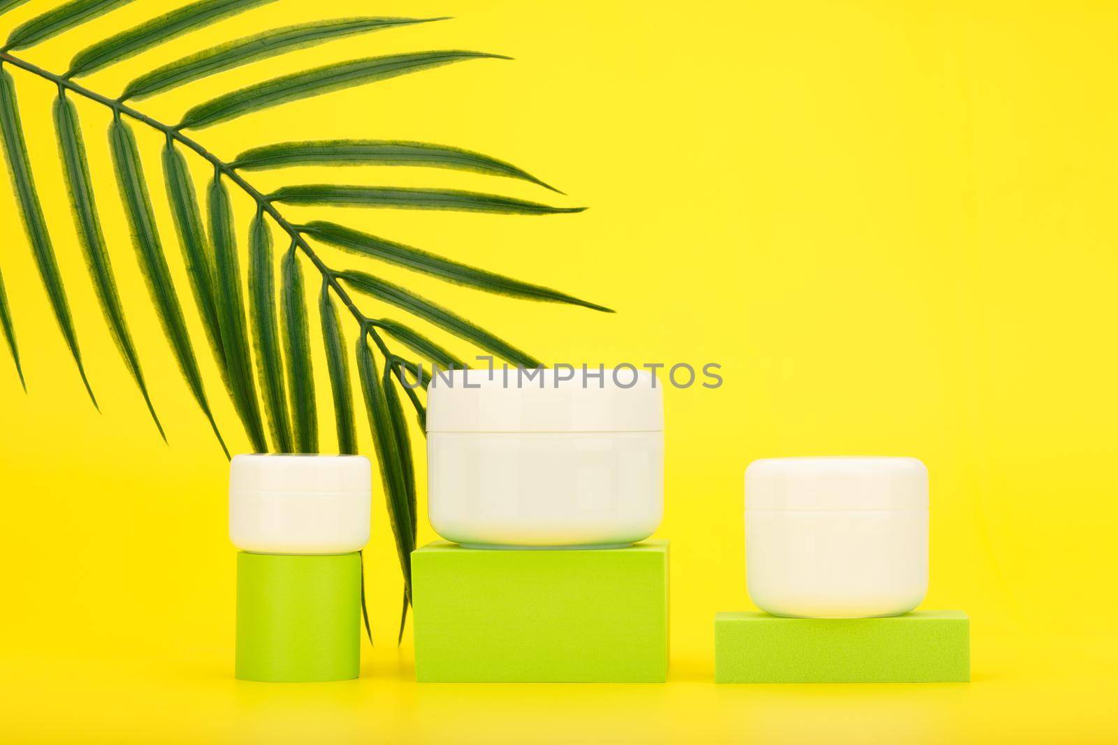Set of cosmetic products with spf factor for skin care during summer. Lip balm, face and under eye cream against yellow background with palm leaf. Concept of beauty products with sunscreen. 