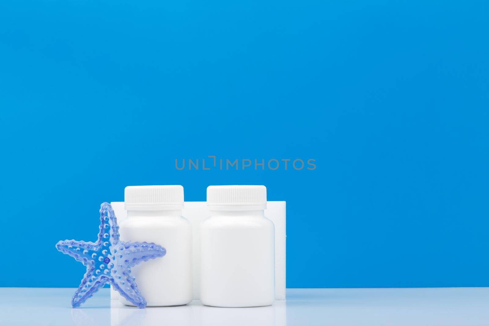 Two medication bottles with sea star against blue background with copy space. Supplements with sea minerals for healthy lifestyle and wellness. Concept of wellness, vitamins and supplements
