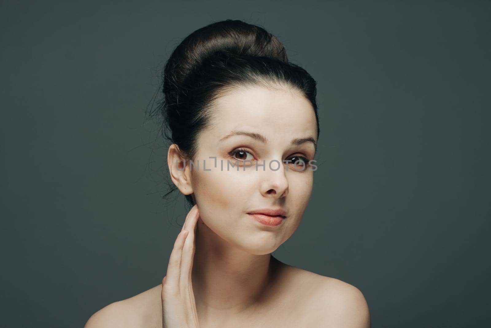 brunette with bare shoulders gathered hair hand near face. High quality photo