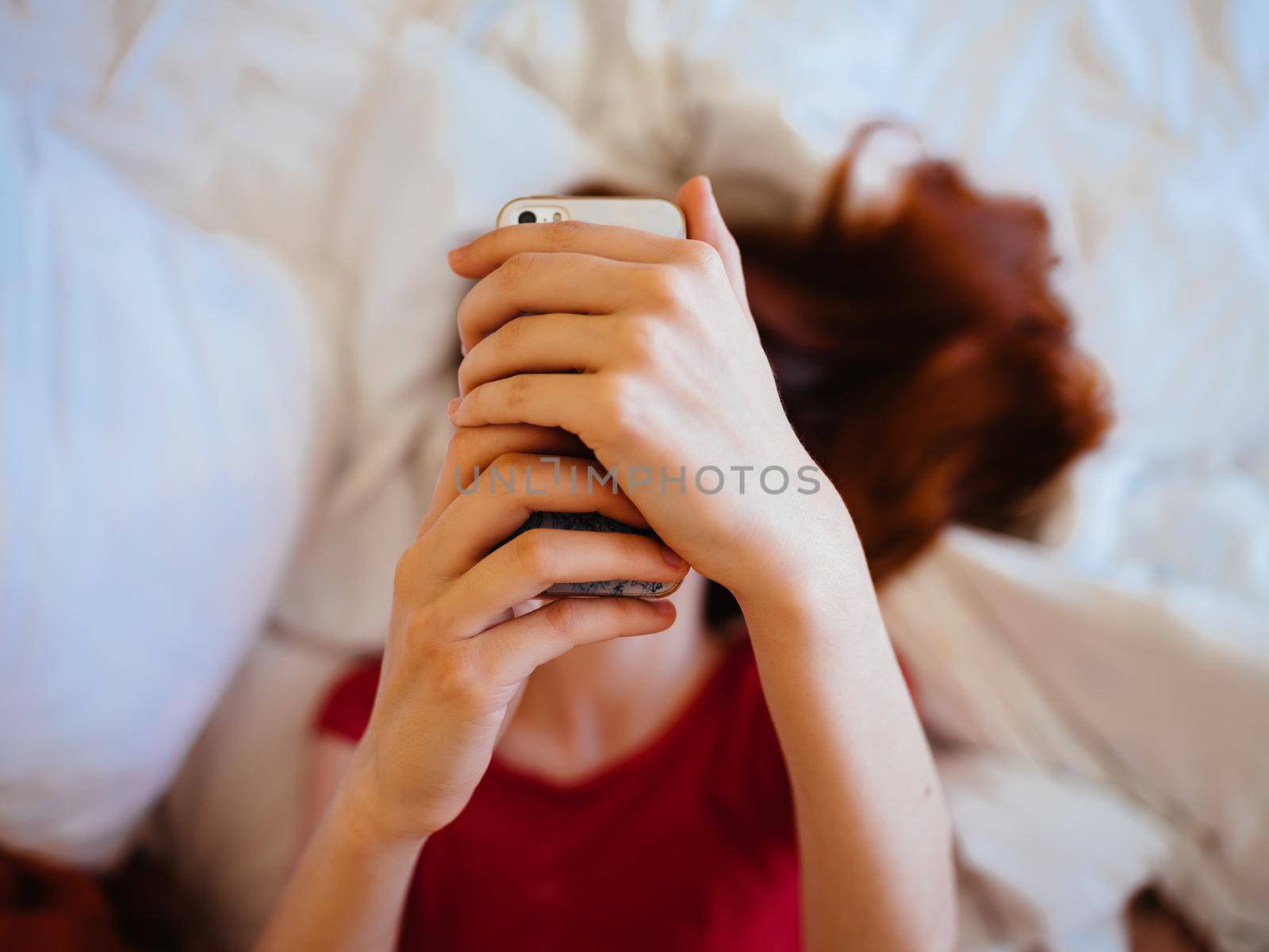 Woman with mobile phone writes message model red t-shirt bed. High quality photo