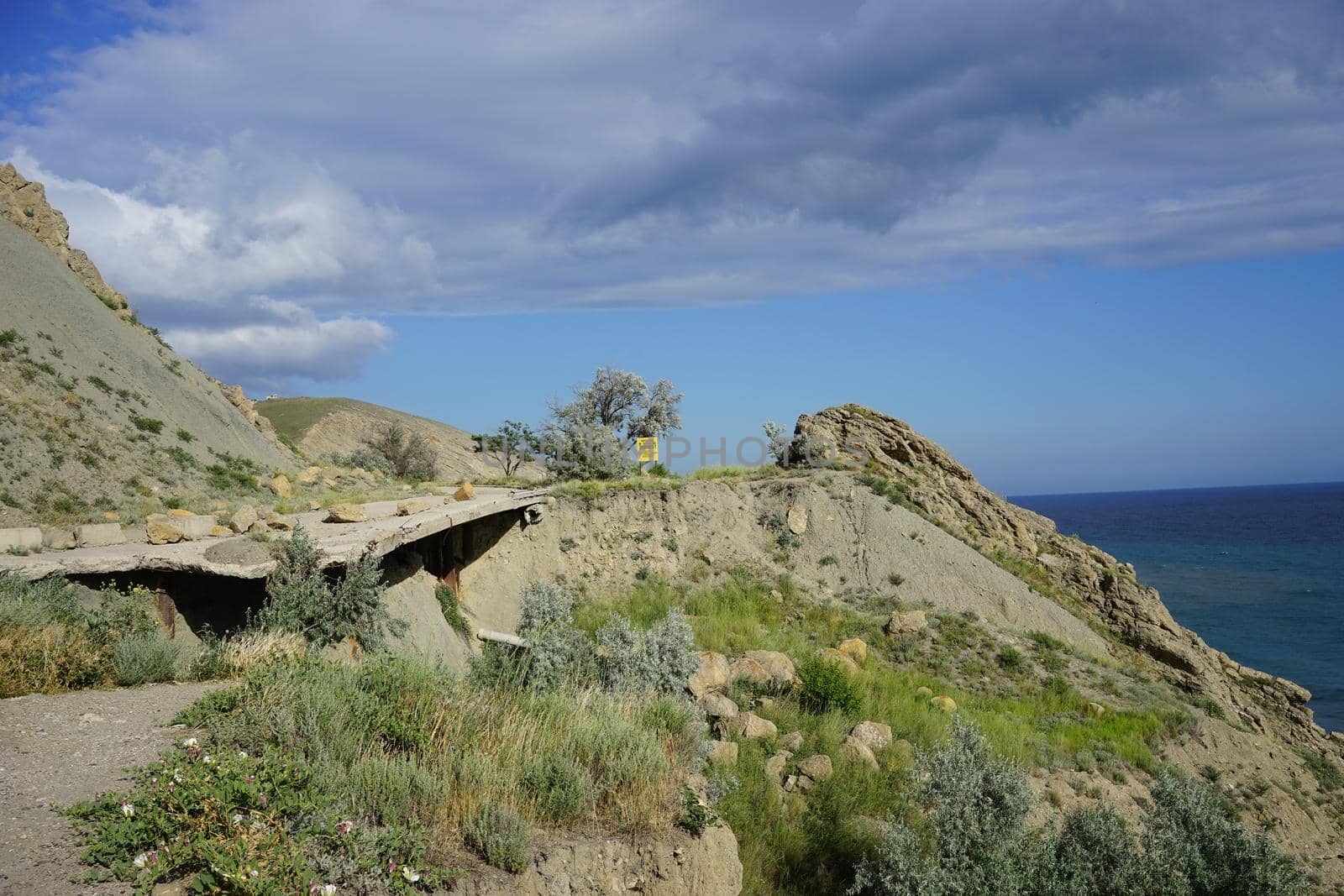 broken road in the middle of the volcanic hills under a bright blue sky with white clouds on a hot summer day