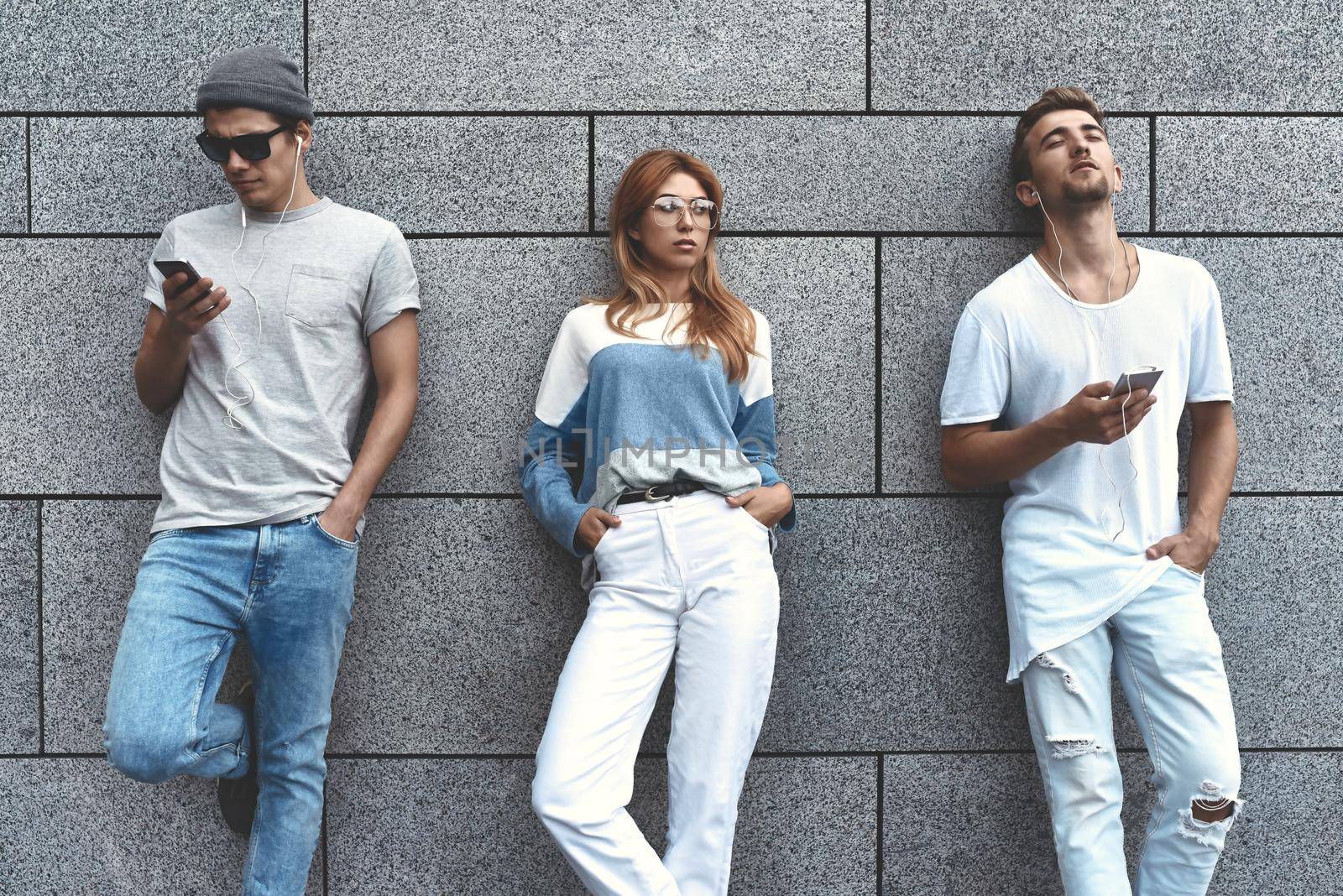 Fashion portrait of Three best friends posing at street, wearing stylish outfit and jeans against gray wall .