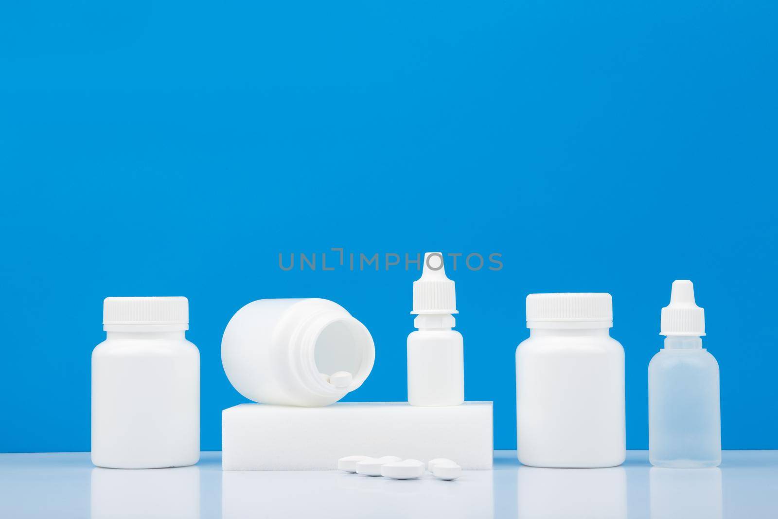 White medication bottles with pills, nose spray and eye drops on white table against blue background with copy space.  by Senorina_Irina