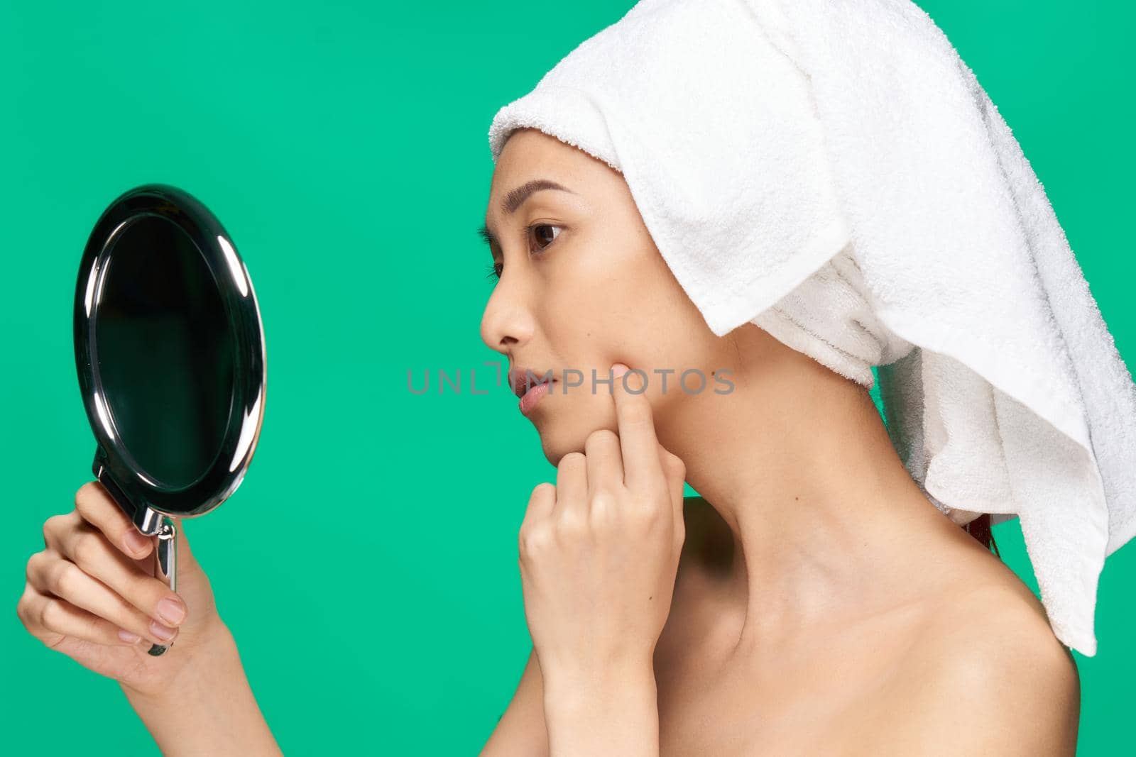 woman of Asian appearance with a towel on her head naked shoulders Looking in the mirror. High quality photo