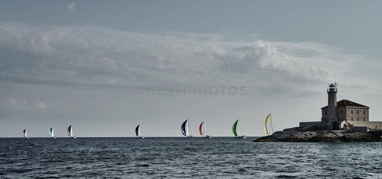 Sailboats compete in a sail regatta at sunset, Boats bend around the island with a beacon, a race, multicolored spinnakers, number of boat is on aft boats, island is on background, clear weather by vladimirdrozdin