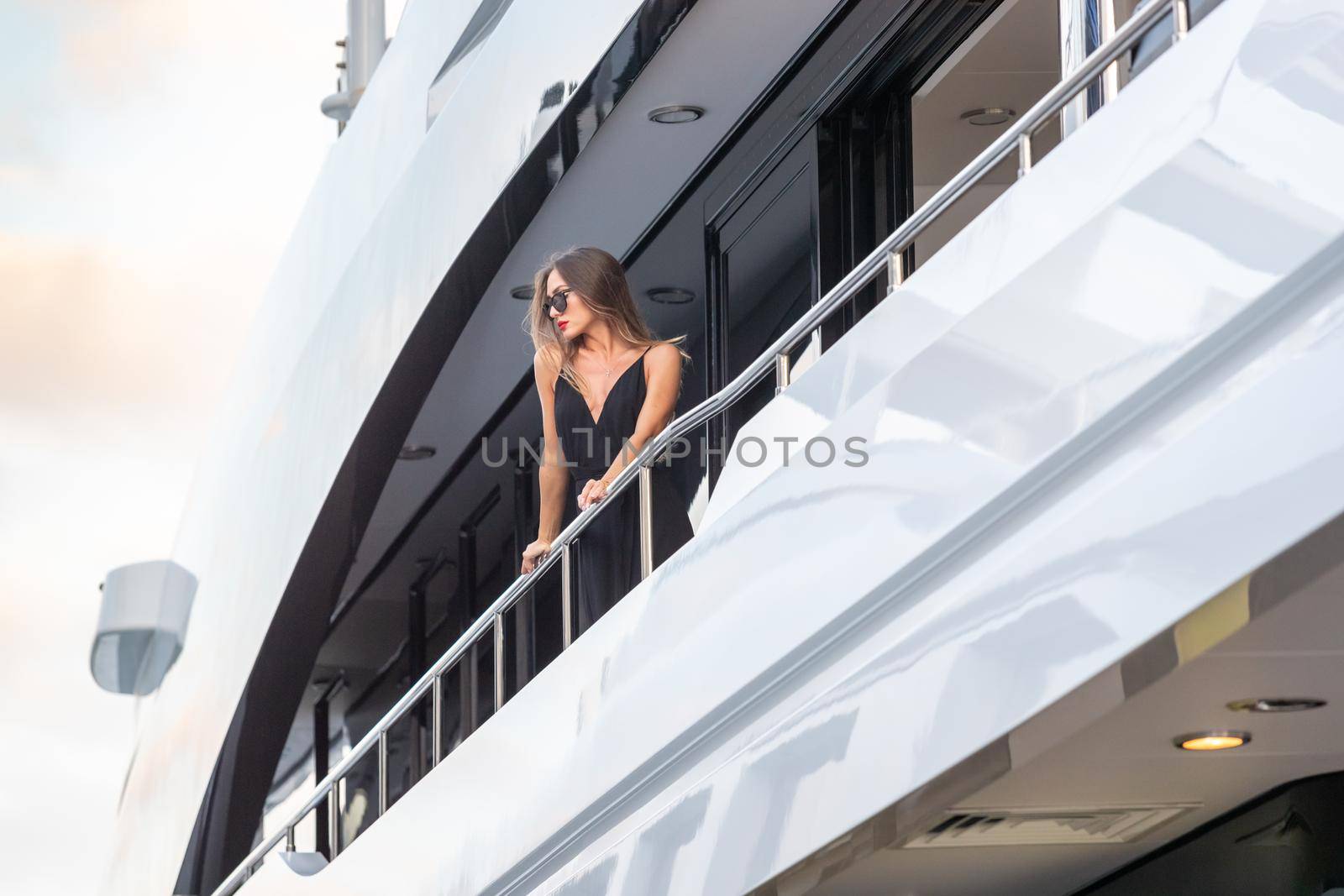 The elegant girl dressed in an evening dress of black color and sunglasses stands on the top deck of a huge yacht in anticipation, red lips, gorgeous lady, she does up hair, Monaco, Monte-Carlo