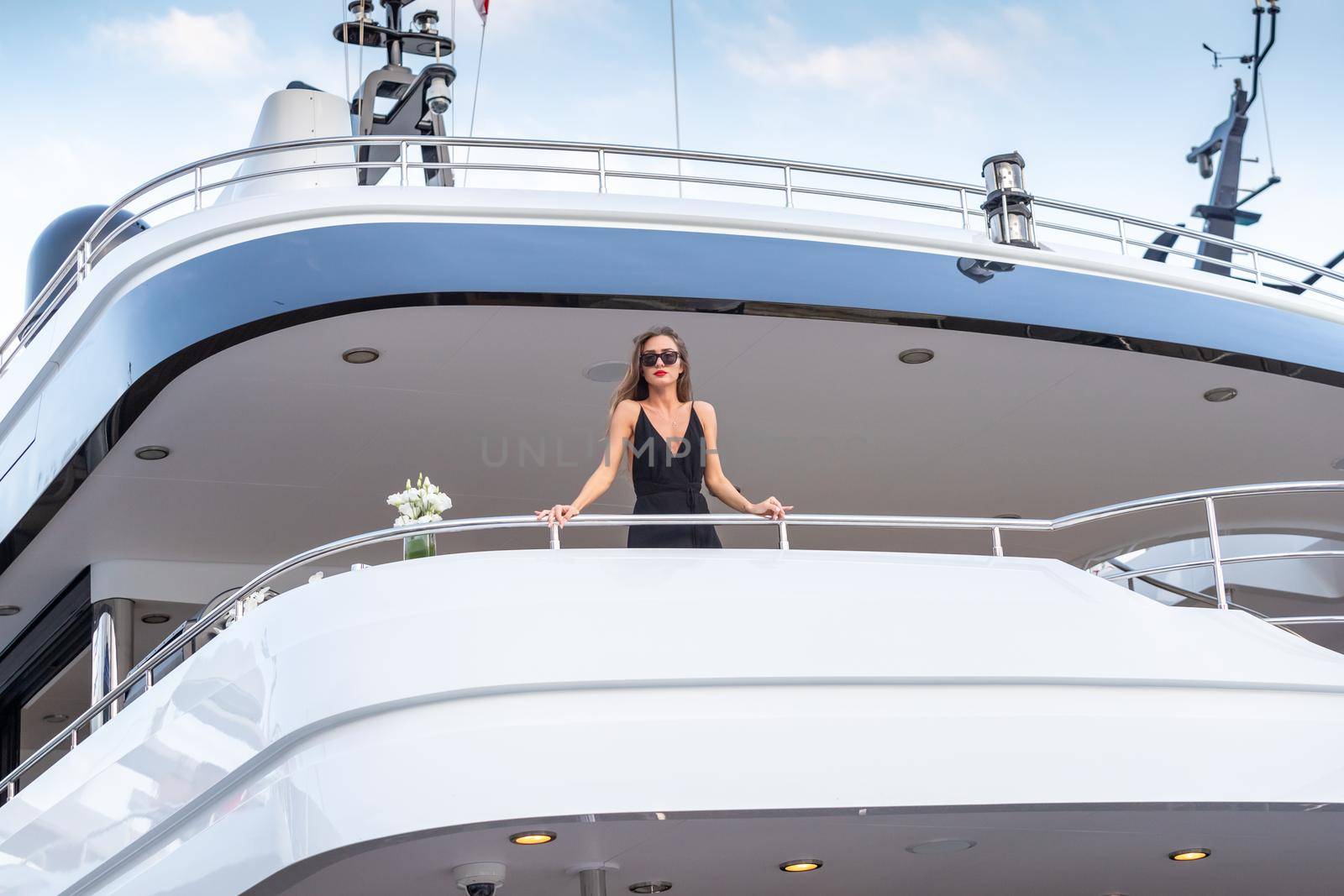 The elegant girl dressed in an evening dress of black color and sunglasses stands on the top deck of a huge yacht in anticipation, red lips, gorgeous lady, she does up hair, Monaco, Monte-Carlo