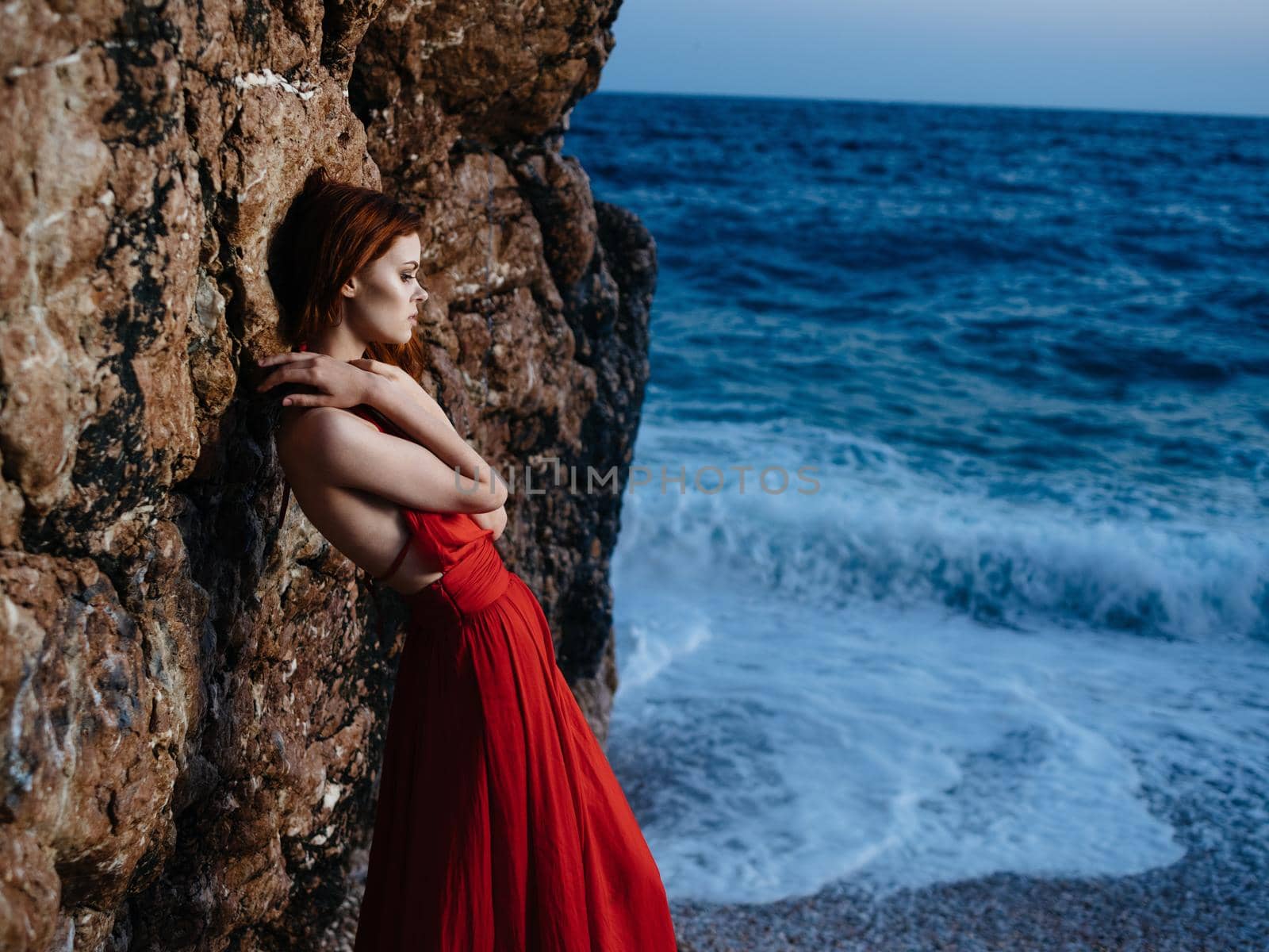 Woman in red dress rocky stone landscape ocean waves. High quality photo