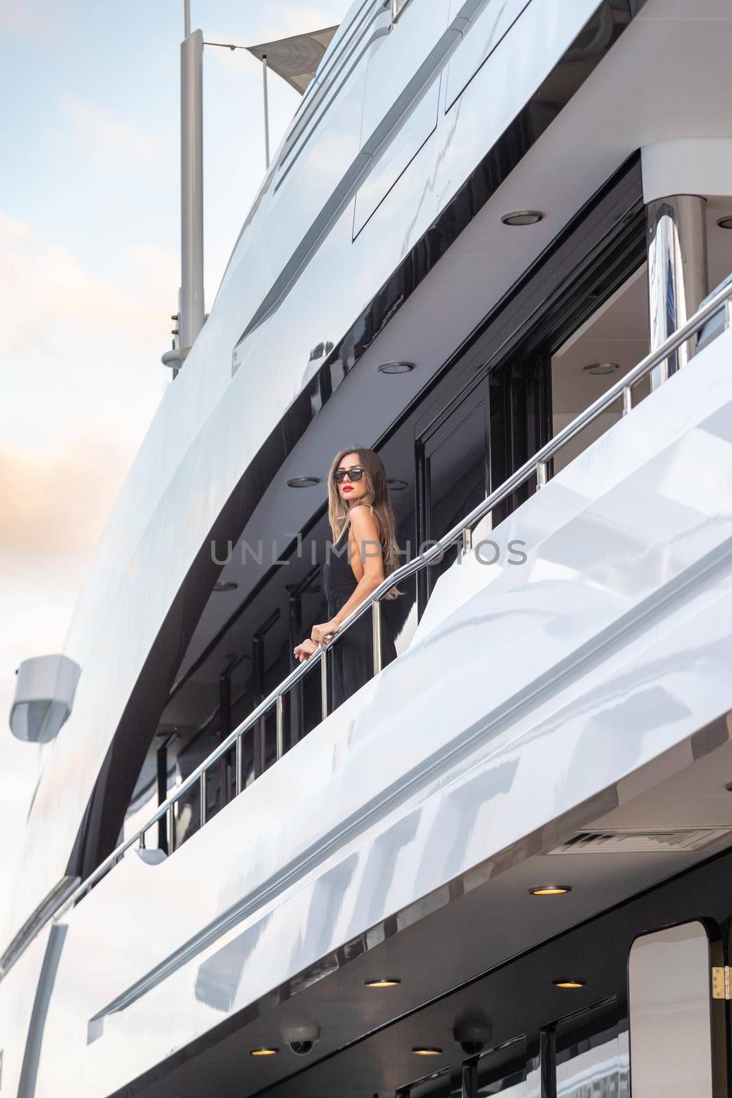 The elegant girl dressed in an evening dress of black color and sunglasses stands on the top deck of a huge yacht in anticipation, red lips, gorgeous lady, she does up hair, Monaco, Monte-Carlo