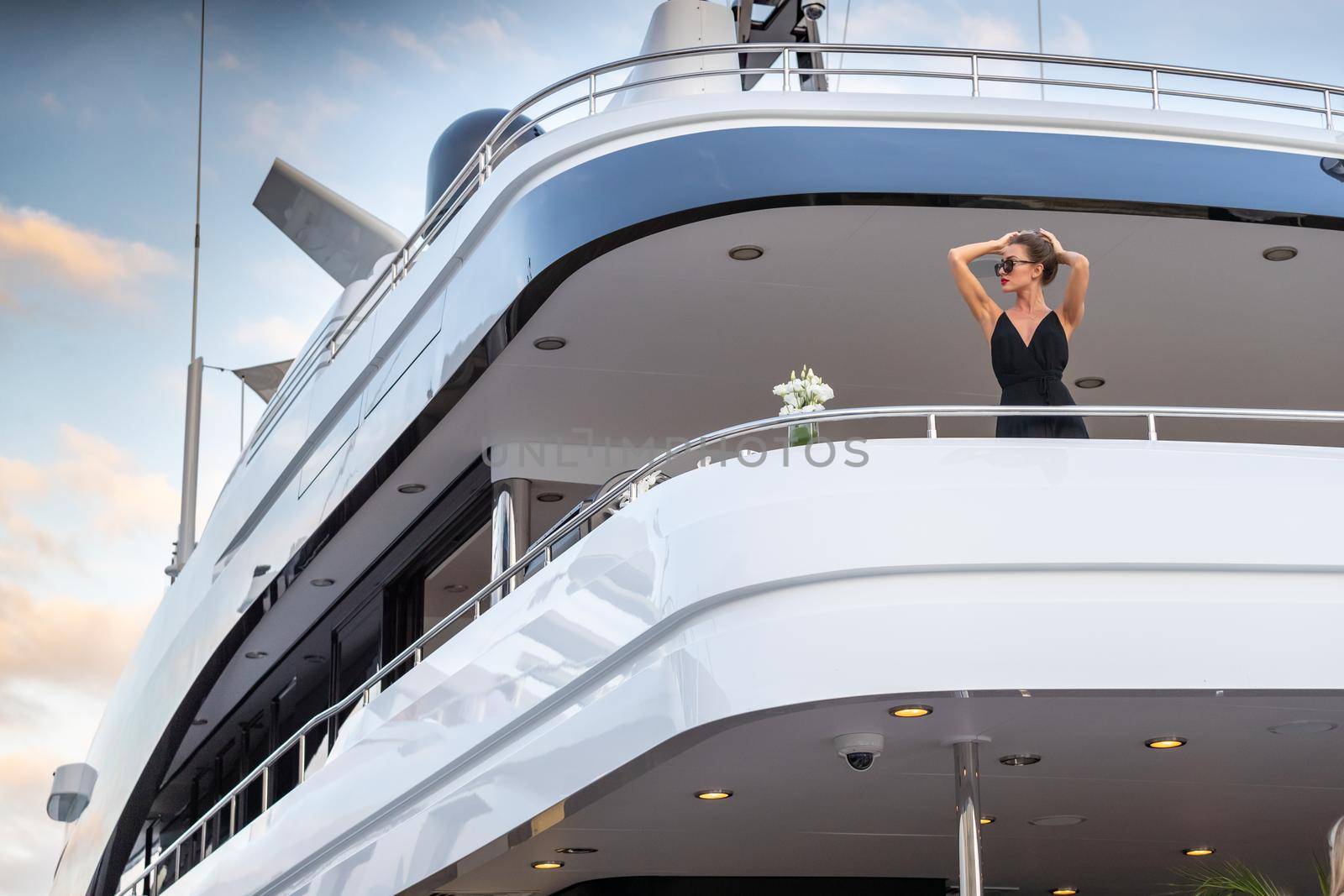 The elegant girl dressed in an evening dress of black color and sunglasses stands on the top deck of a huge yacht in anticipation, red lips, gorgeous lady, she does up hair, Monaco, Monte-Carlo