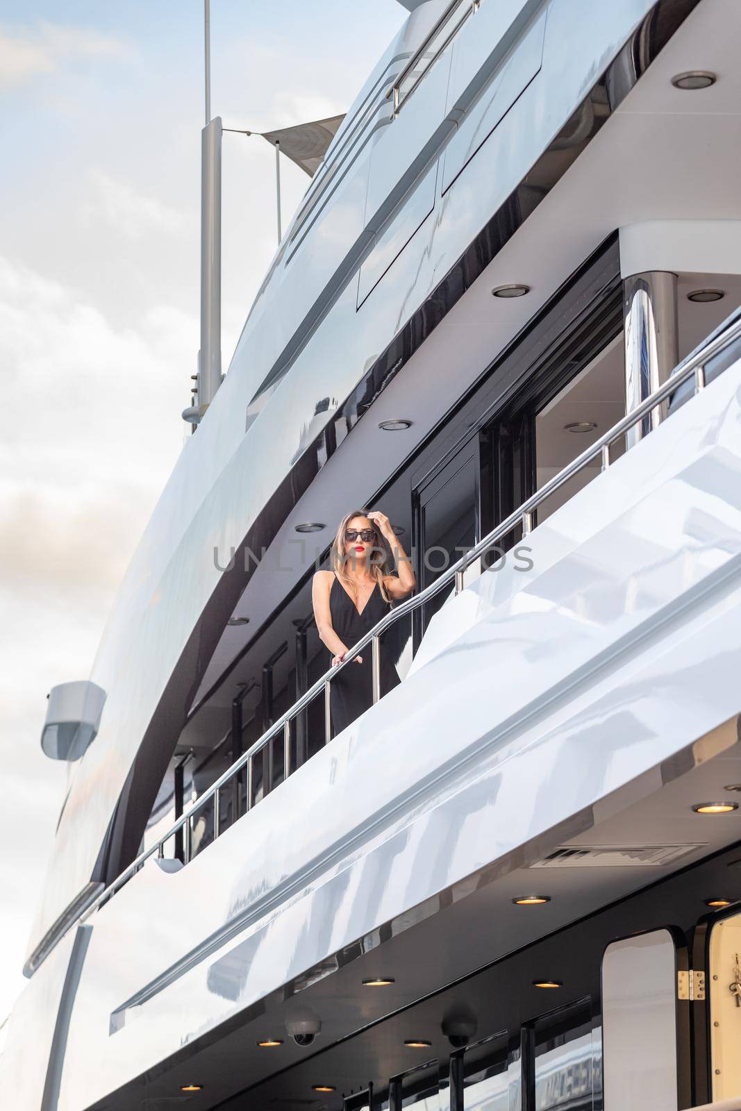 The elegant girl dressed in an evening dress of black color and sunglasses stands on the top deck of a huge yacht in anticipation, red lips, gorgeous lady, she does up hair, Monaco, Monte-Carlo