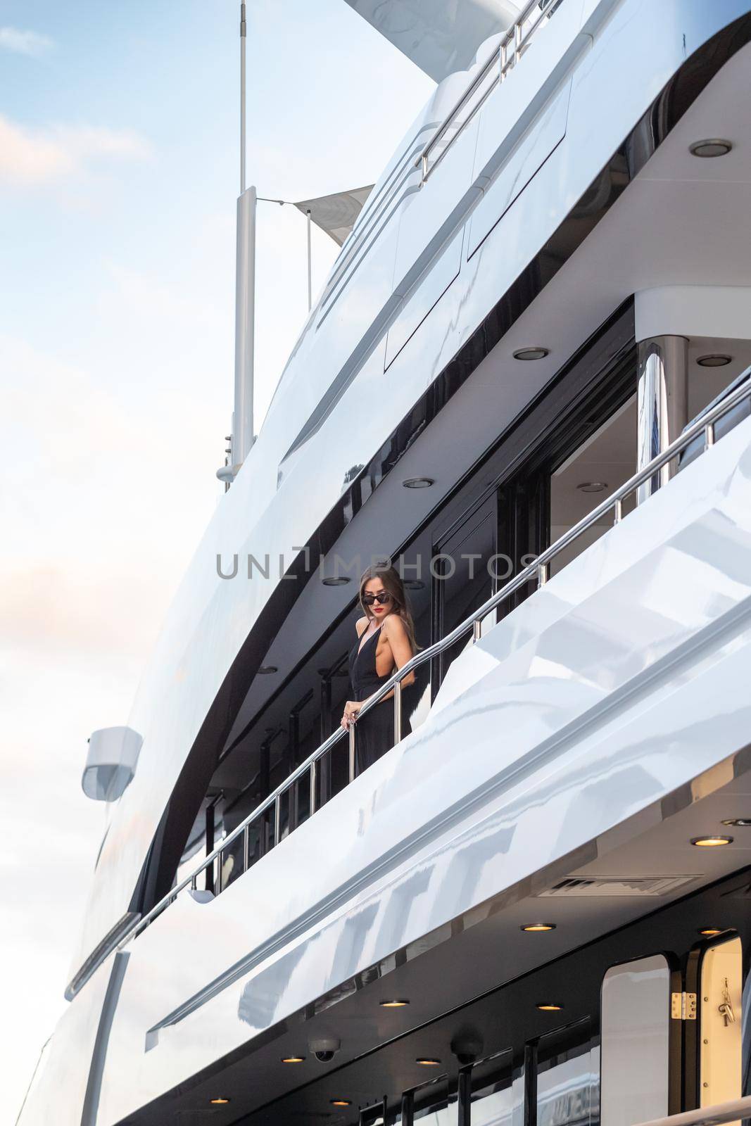 The elegant girl dressed in an evening dress of black color and sunglasses stands on the top deck of a huge yacht in anticipation, red lips, gorgeous lady, she does up hair, Monaco, Monte-Carlo