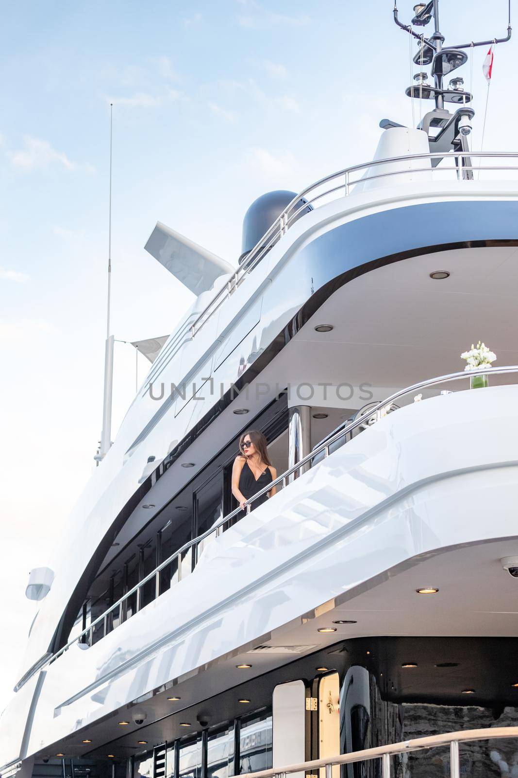 The elegant girl dressed in an evening dress of black color and sunglasses stands on the top deck of a huge yacht in anticipation, red lips, gorgeous lady, she does up hair by vladimirdrozdin