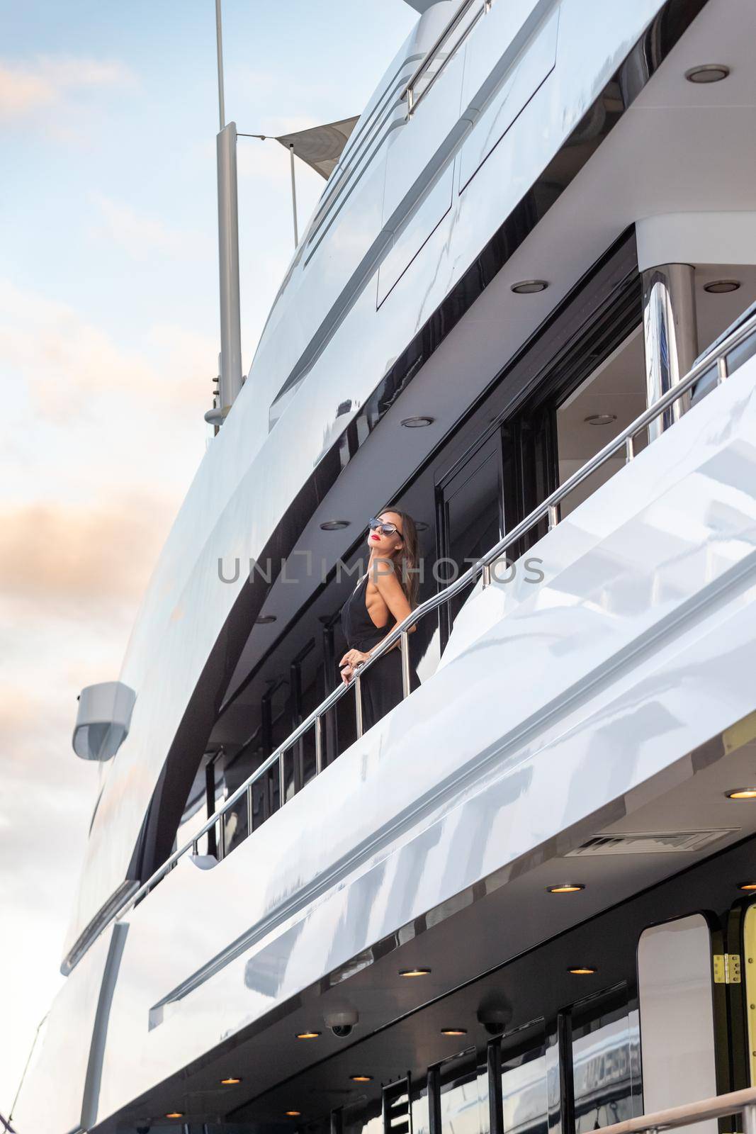 The elegant girl dressed in an evening dress of black color and sunglasses stands on the top deck of a huge yacht in anticipation, red lips, gorgeous lady, she does up hair, Monaco, Monte-Carlo