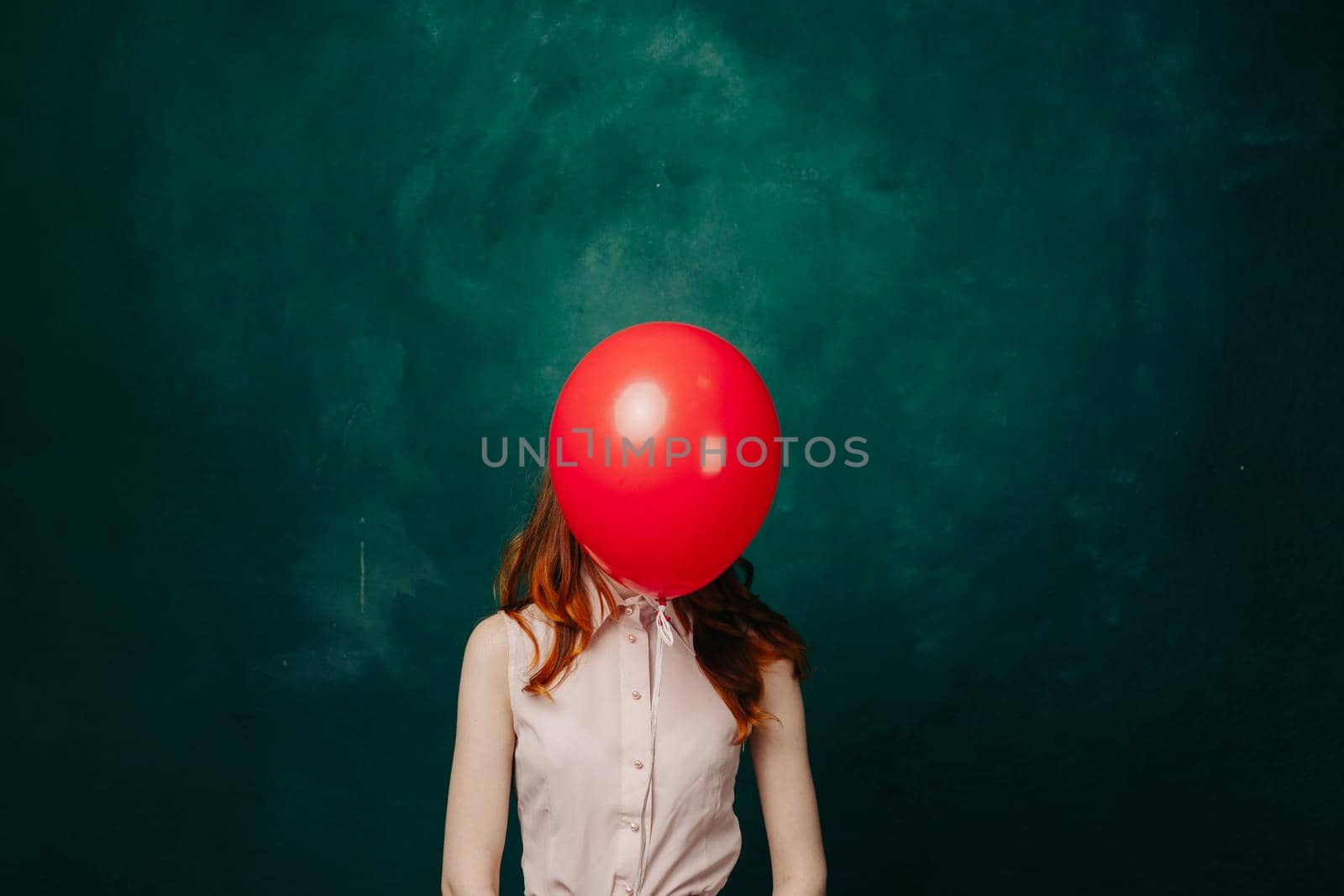 woman with red ball in front of face on green background in pink dress cropped view. High quality photo