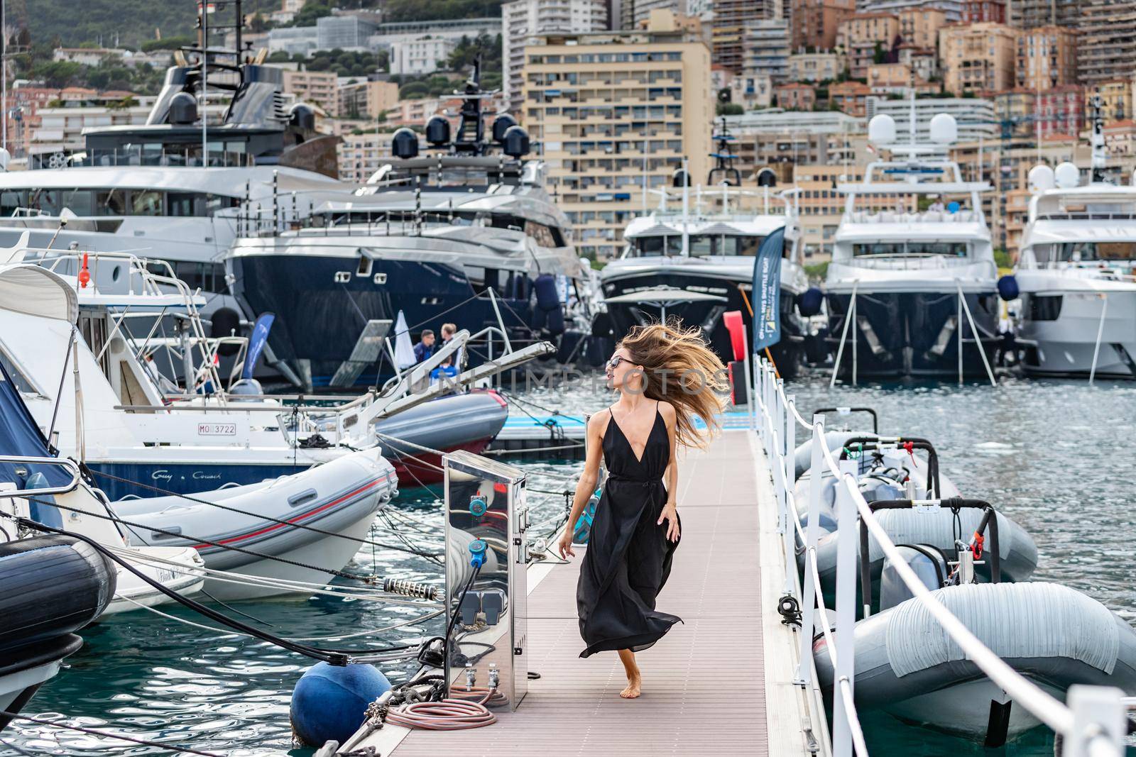 Monaco, Monte-Carlo, 27 September 2019: The elegant girl dressed in an evening dress of black color and sunglasses runs on pier in Monaco Yacht Show, gorgeous woman, sexual red lips, people