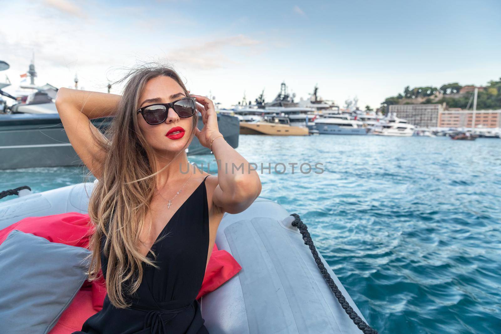 The elegant girl dressed in an evening dress of black color and sunglasses on the boat carry to the big yacht, gorgeous woman, sexual red lips, Decollete, Monaco, Monte-Carlo by vladimirdrozdin