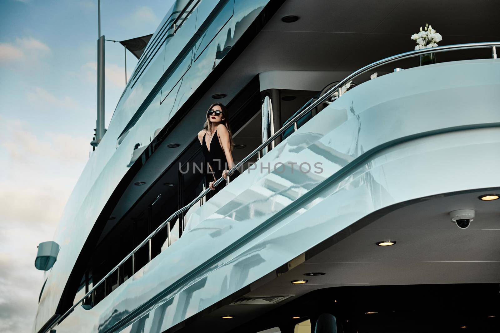 A glamorous diva in an evening dress of black color and sunglasses stands on the top deck of a huge yacht in anticipation, port Hercule, Monaco