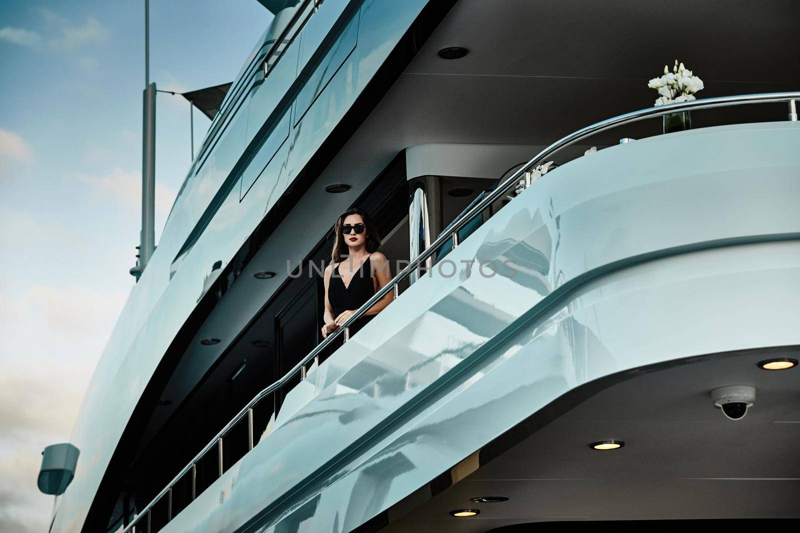 A glamorous diva in an evening dress of black color and sunglasses stands on the top deck of a huge yacht in anticipation, port Hercule, Monaco