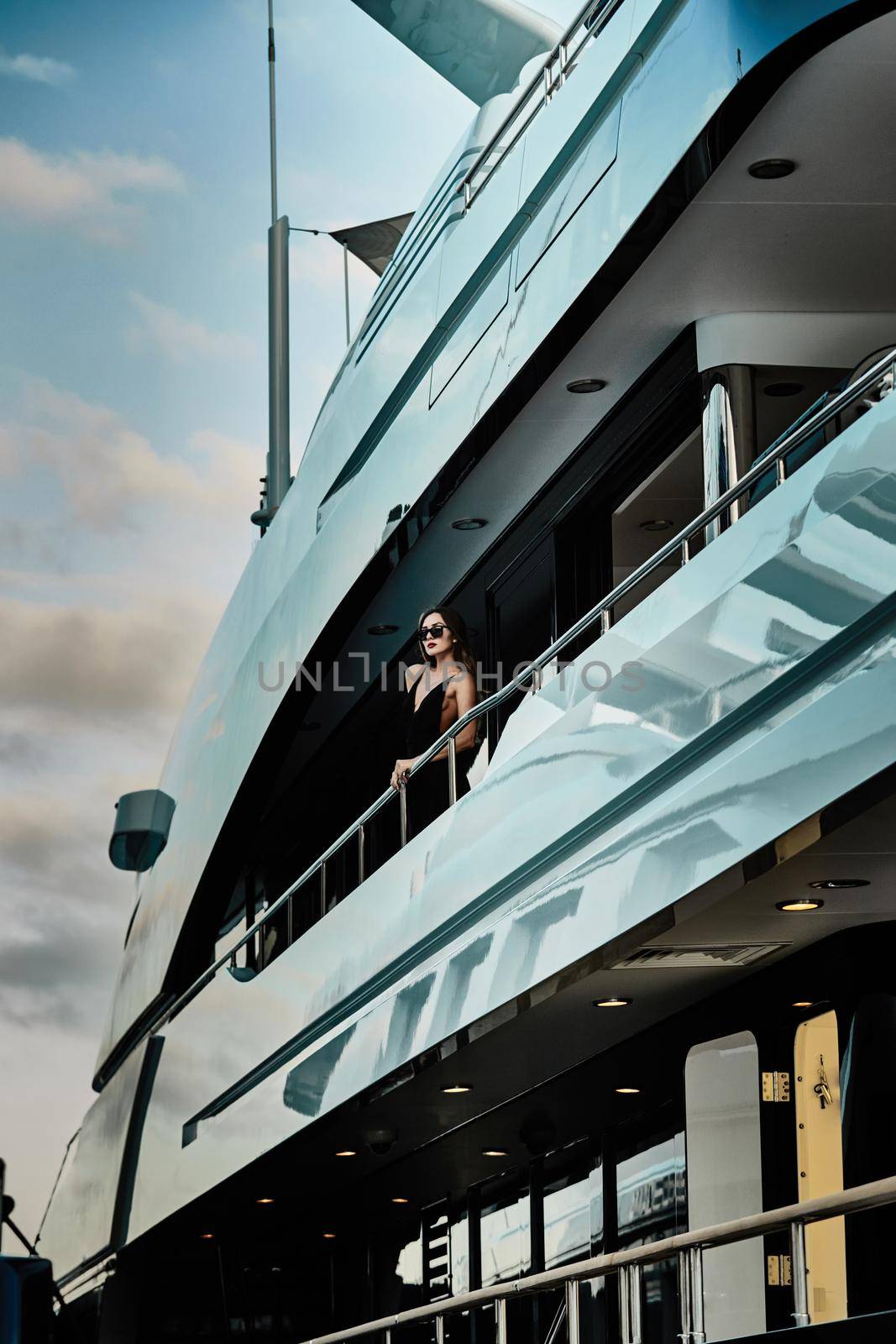 A glamorous diva in an evening dress of black color and sunglasses stands on the top deck of a huge yacht in anticipation, port Hercule, Monaco