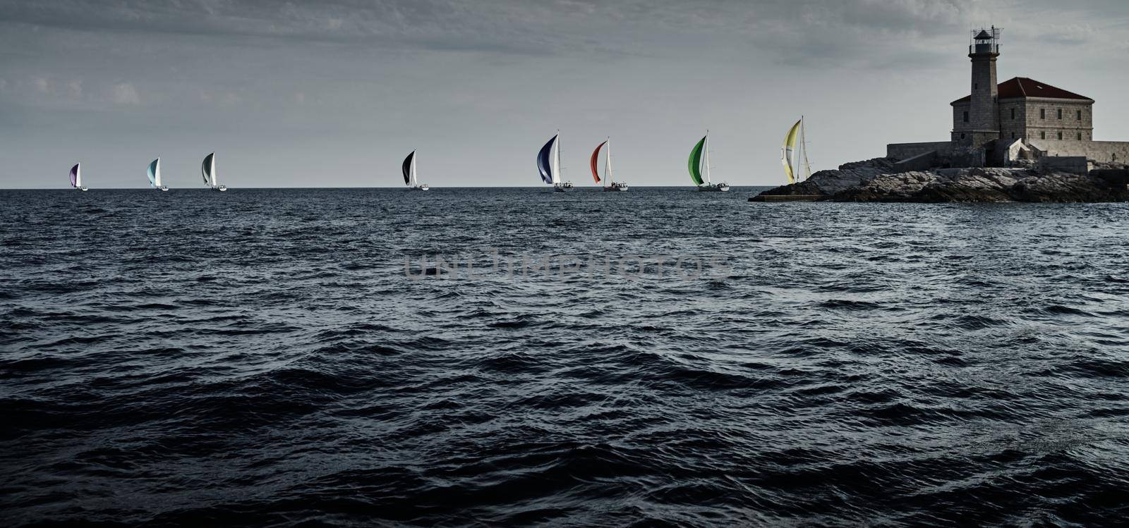 Sailboats compete in a sail regatta at sunset, Boats bend around the island with a beacon, a race, multicolored spinnakers, number of boat is on aft boats, island is on background, clear weather by vladimirdrozdin