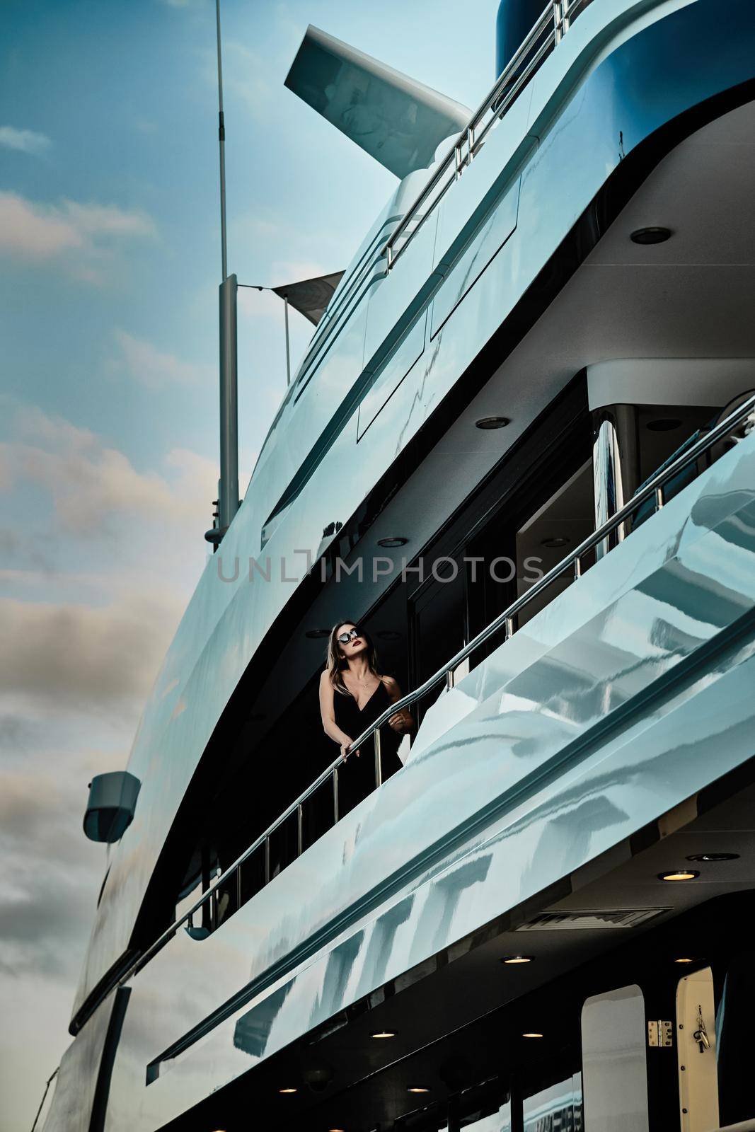 Monaco, Monte-Carlo, 27 September 2019: A glamorous diva in an evening dress of black color and sunglasses stands on the top deck of a huge yacht in anticipation by vladimirdrozdin