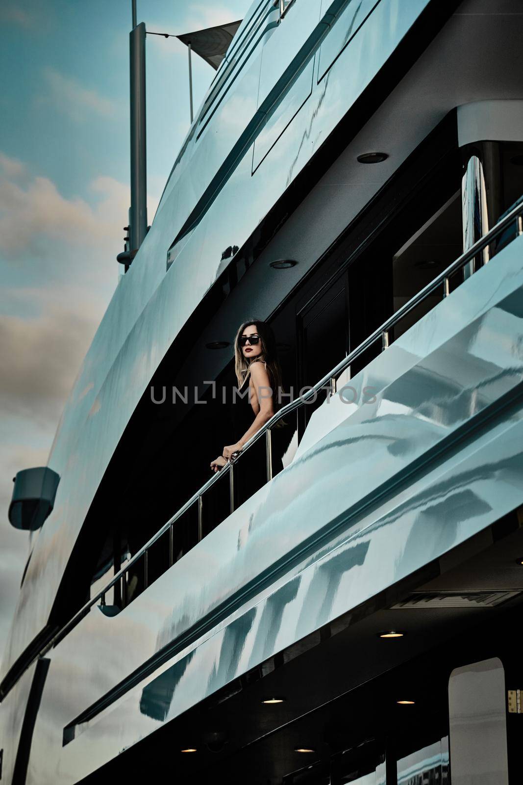 A glamorous diva in an evening dress of black color and sunglasses stands on the top deck of a huge yacht in anticipation by vladimirdrozdin