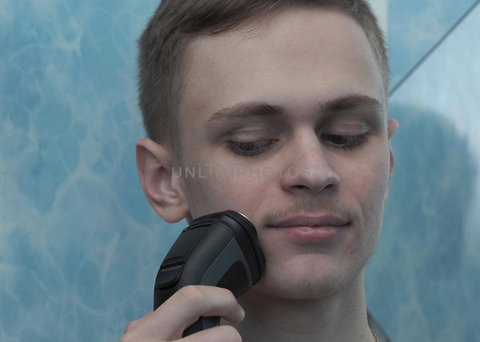 A young man of European appearance shaves an electric razor. Facial. High quality photo