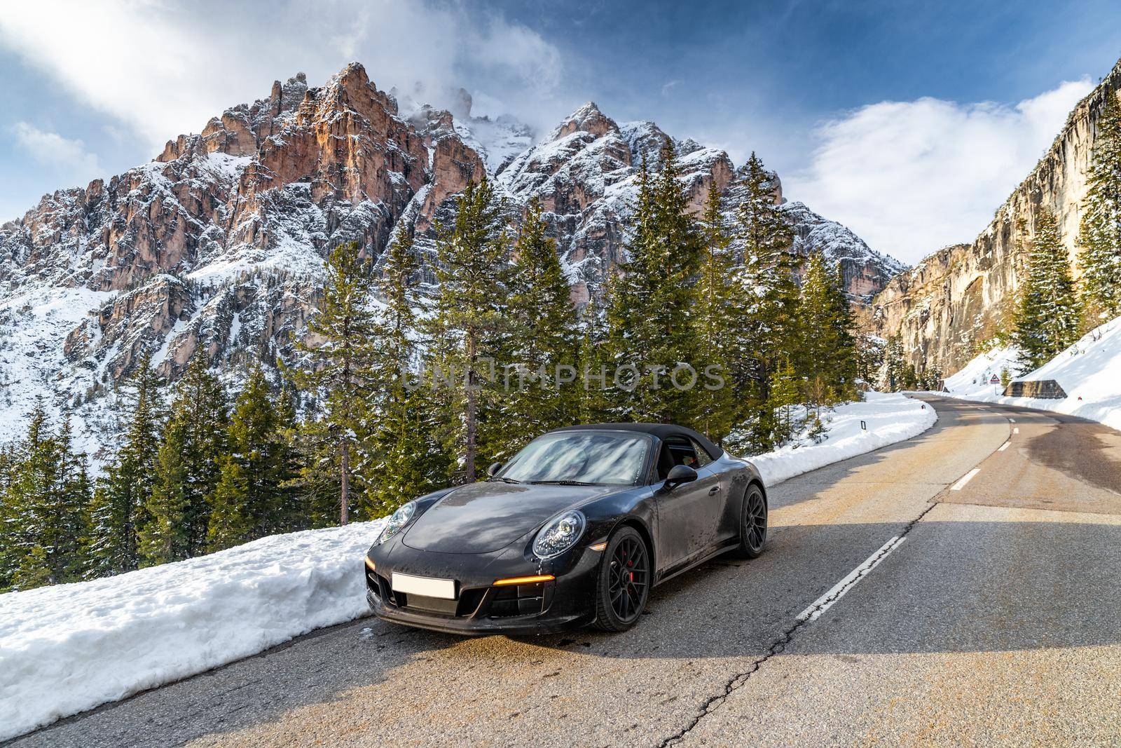 Italy, The Dolomites, Canazei, The expensive luxury sport car a stops on the twisted road against snow-covered mountains Dolomites, monument UNESCO, sunny weather by vladimirdrozdin