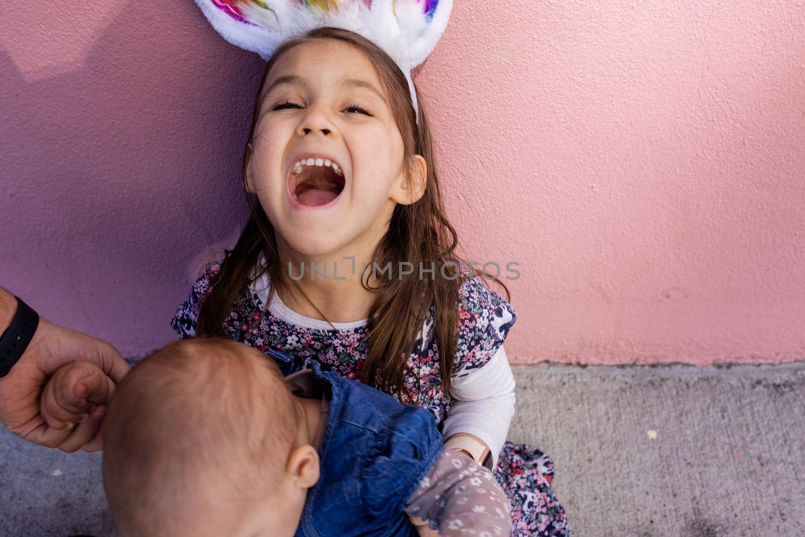 Adorable little girl wearing unicorn headband hugging and kissing a baby by Kanelbulle