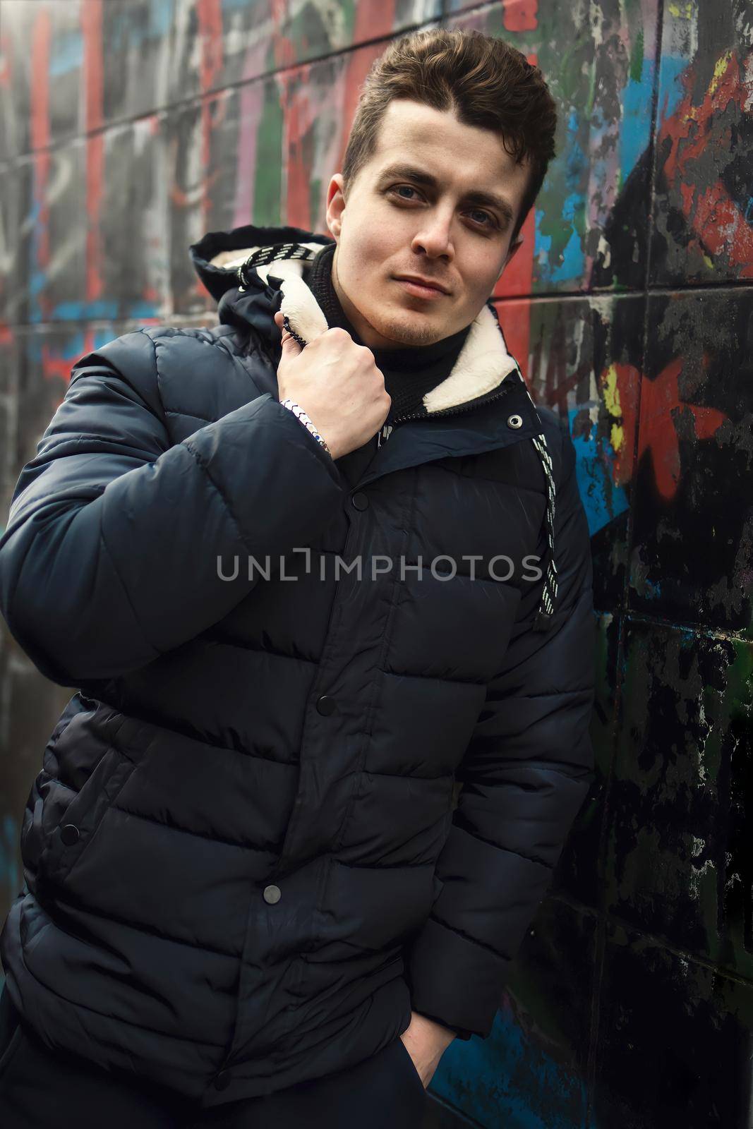 Attractive confident young brunet man standing against graffiti wall and looking into the camera by Nickstock