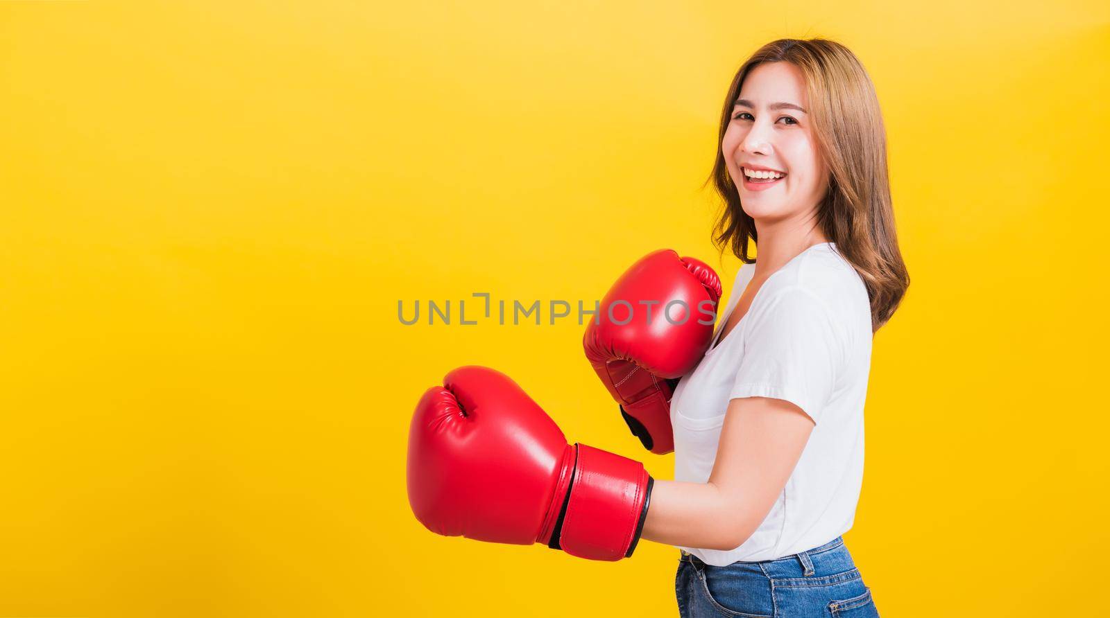 Portrait Asian Thai beautiful young woman standing smile wearing red boxing gloves she poses like a boxer, studio shot isolated on yellow background, There was copy space for text