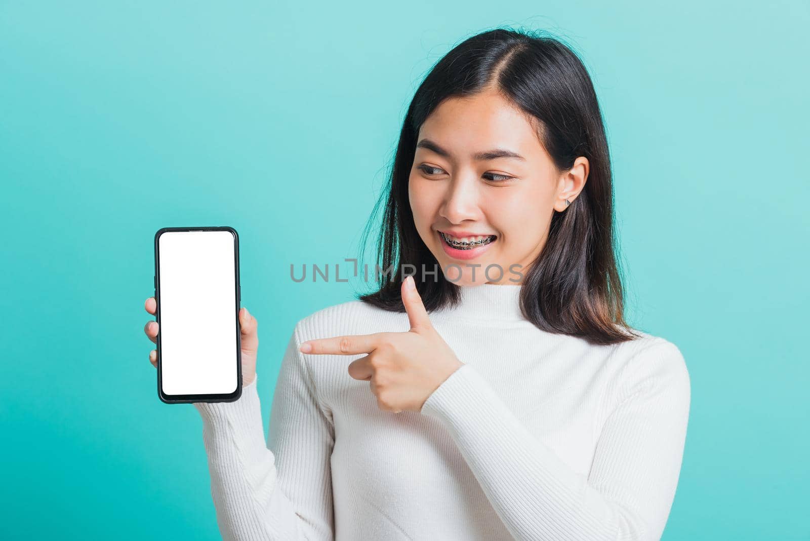 woman smile holding a smartphone on hand and pointing finger to the blank screen by Sorapop
