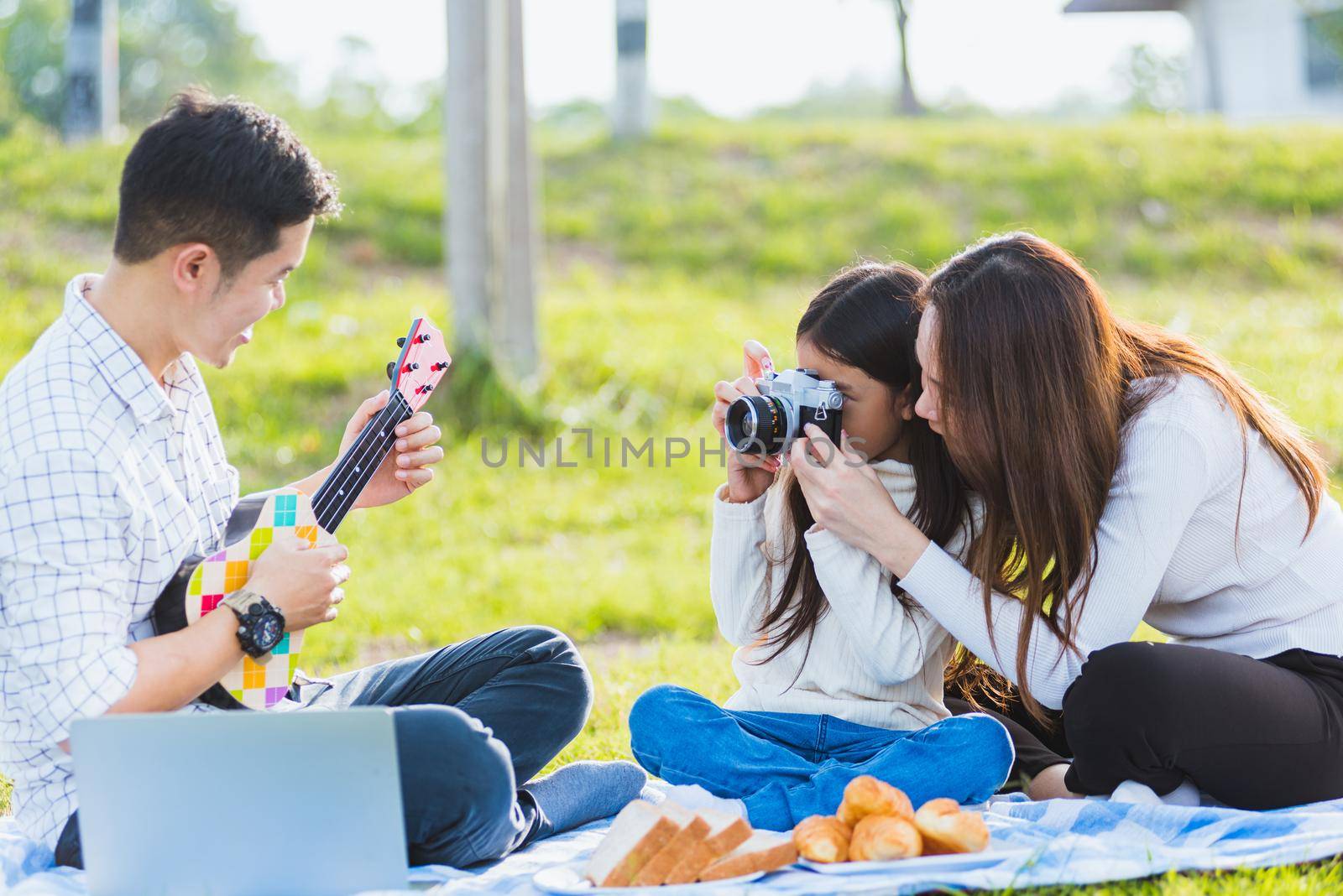 family father, mother and child having fun and enjoying outdoor together sitting on the grass party with shooting photos by Sorapop