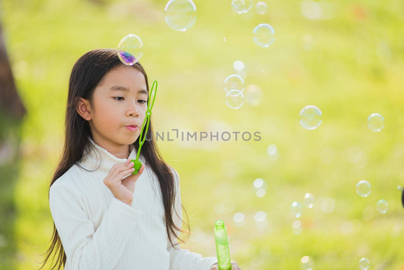 little cute girl child having fun and enjoying outdoor play blowing soap bubbles by Sorapop