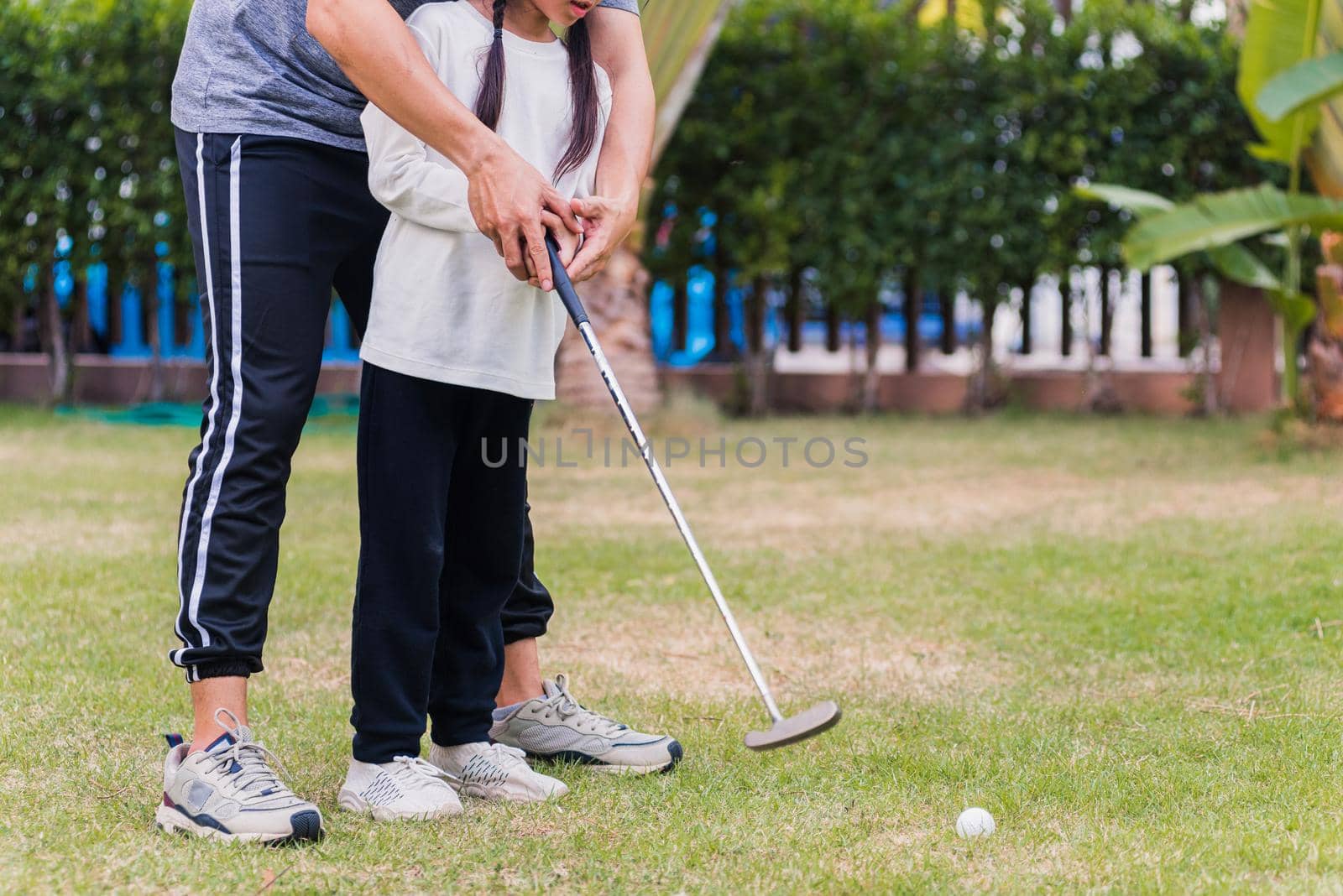 Asian young father support teaching training daughter to play perfect golf while standing in the game of golf together in nature a field garden park, family outdoors sport concept