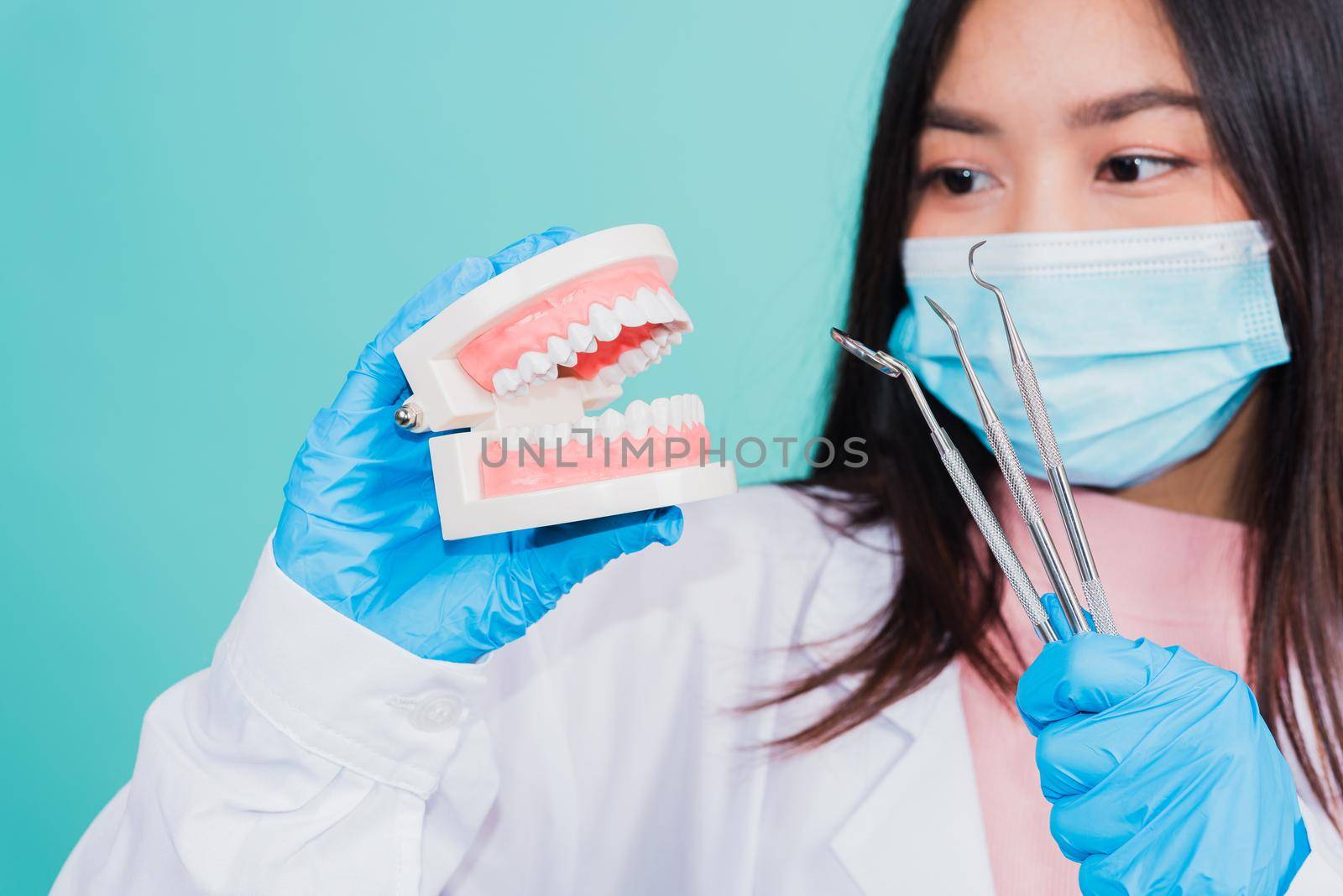 Asian beautiful woman dentist holding professional tool and model teeth denture, female doctor checking denture studio shot isolated on blue background. Dental hygiene surgery health care concept