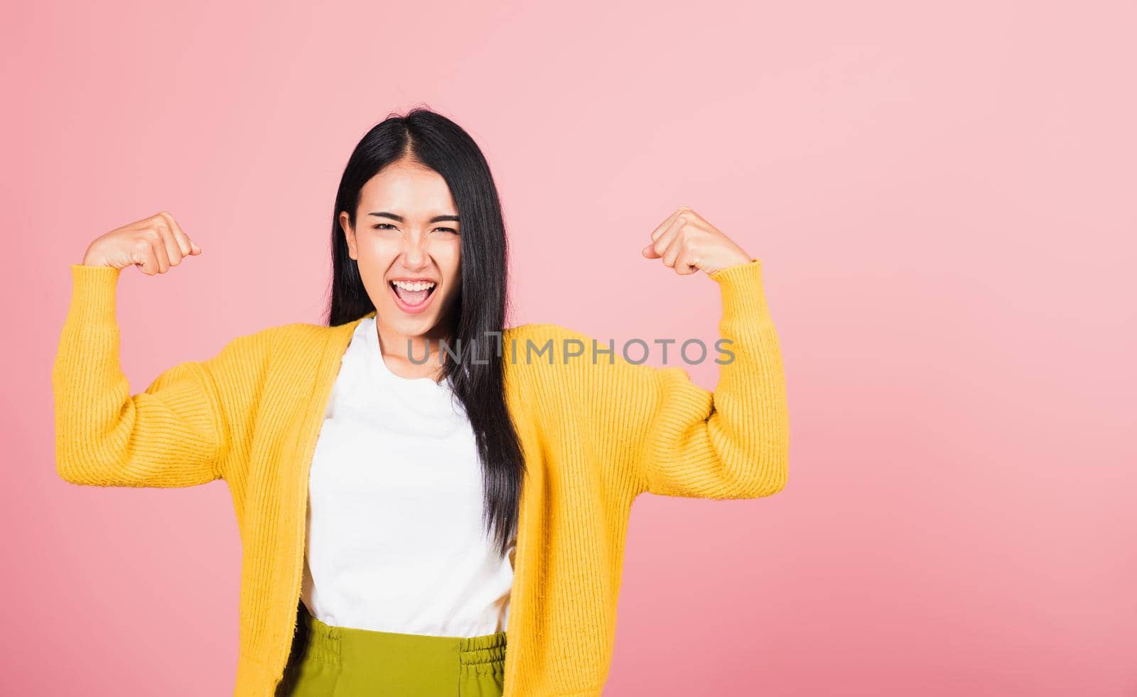 Portrait Asian of happy beautiful strong muscles young woman raises arms biceps confident showing power and strength have feeling independent victory successful, studio shot isolated pink background