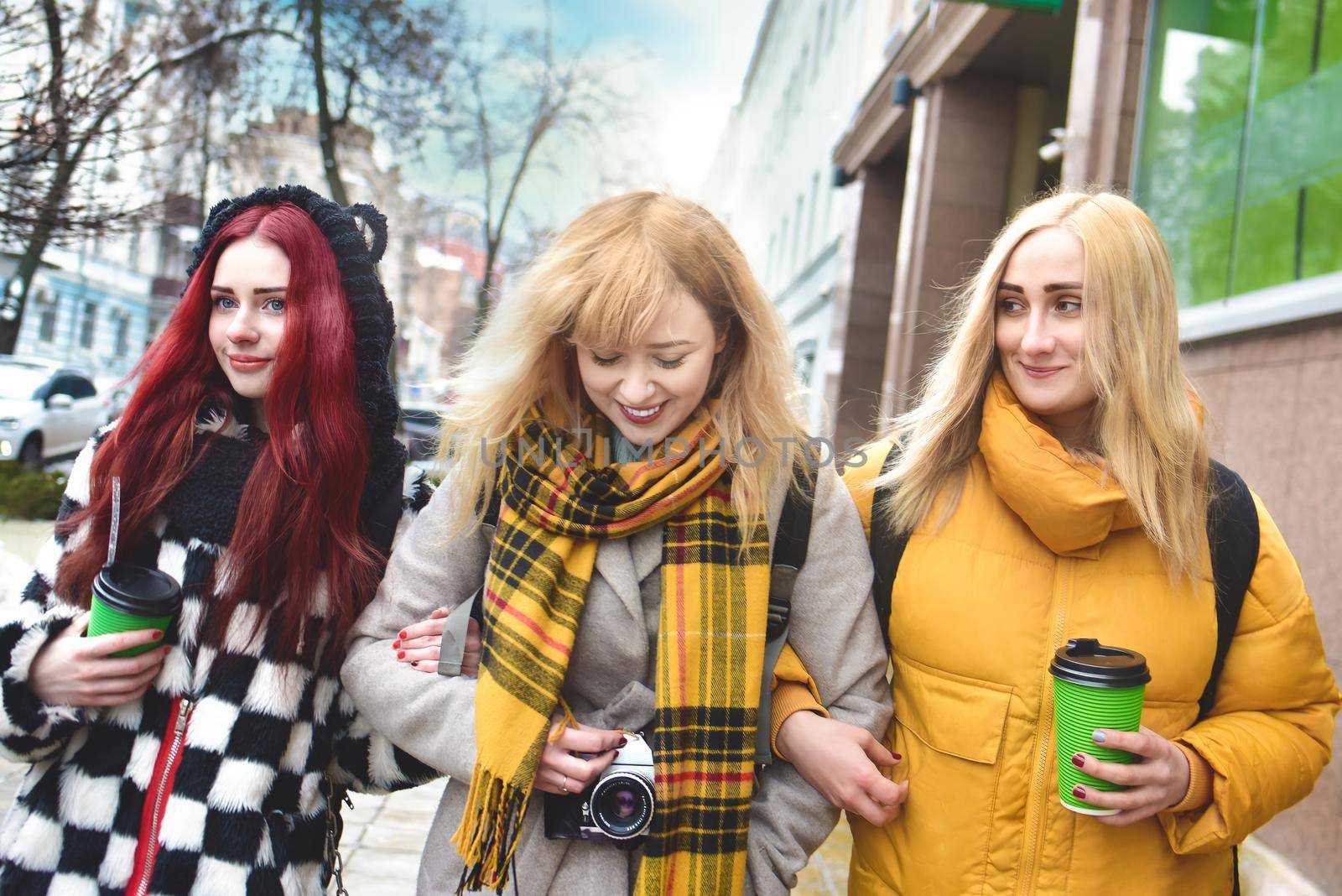 Vacation, tourism concept - three student beautiful girls walking around the city drinking coffee and and taking pictures
