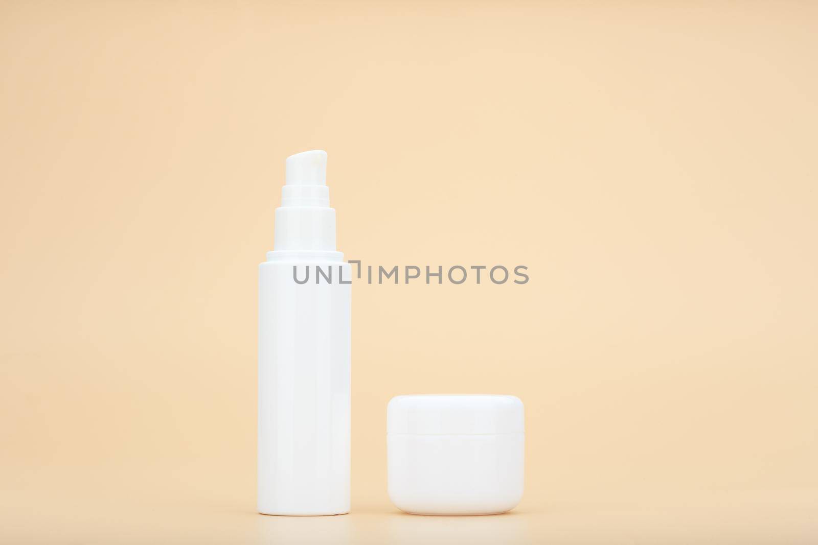 Minimalistic still life with unbranded white tube with beauty product, face cream, serum or lotion and white jar with mask or scrub for daily skin care routine against beige background with copy space
