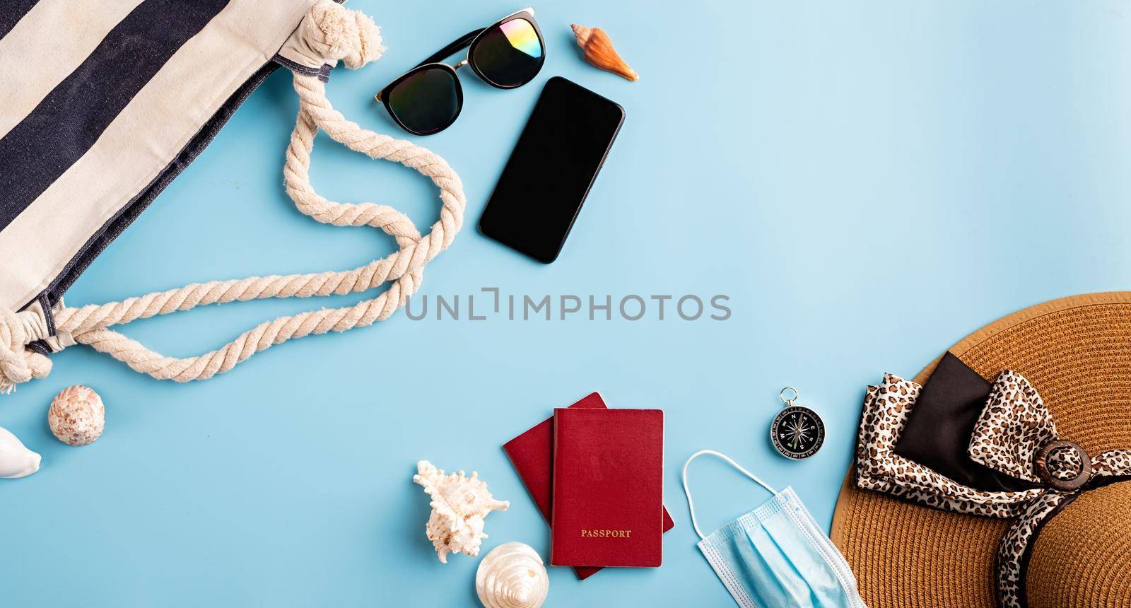 Flat lay travelling objects with summer hat, smartphone, passport, sunglasses and compass on blue background by Desperada