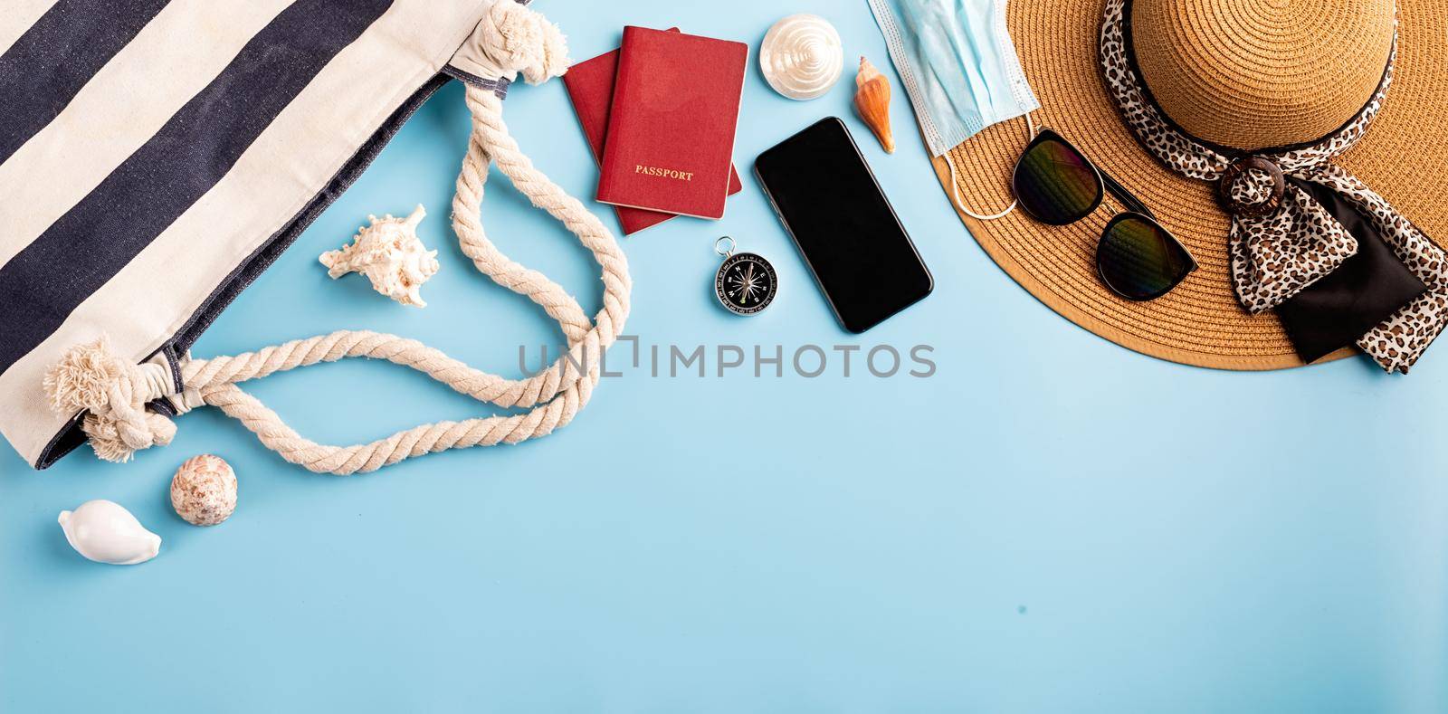Flat lay travelling objects with summer hat, smartphone, passport, sunglasses and compass on blue background by Desperada