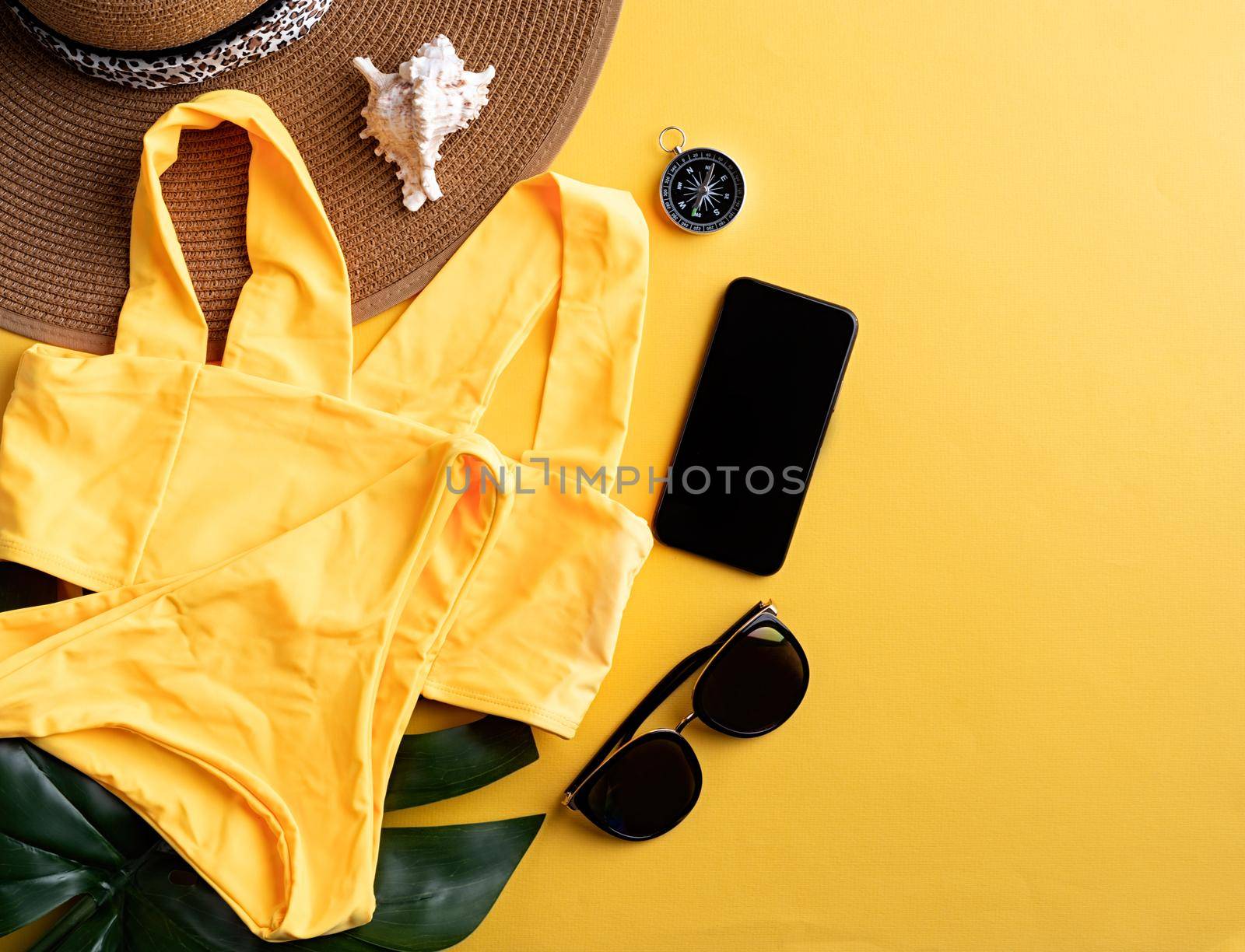 Travel and adventure. Flat lay travelling gear with swimsuit, smartphone, sunglasses and compass on yellow background with copy space