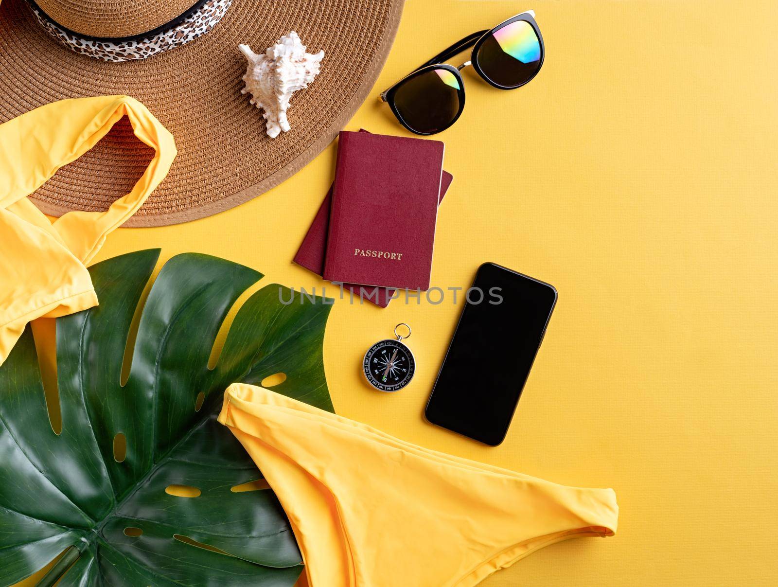 Flat lay travelling gear with swimsuit, passports, smartphone, sunglasses and compass on yellow background by Desperada