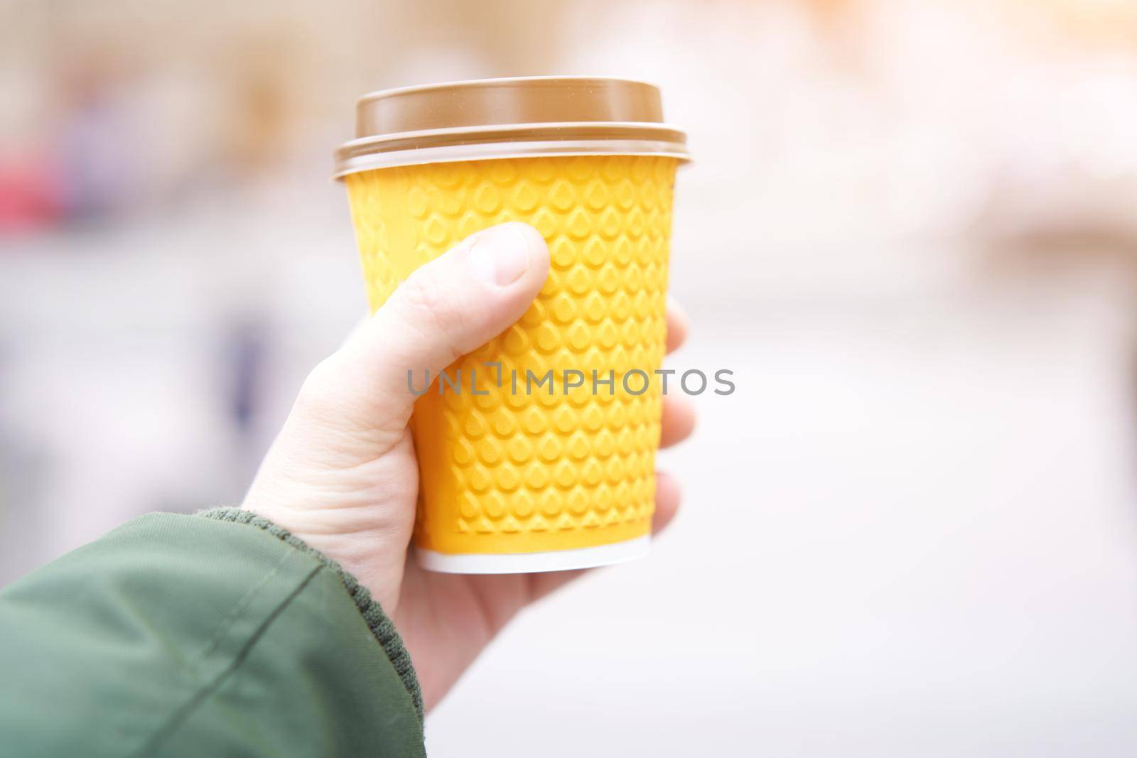 unrecognizable man holding yellow paper cup with coffee in hand on blured street background
