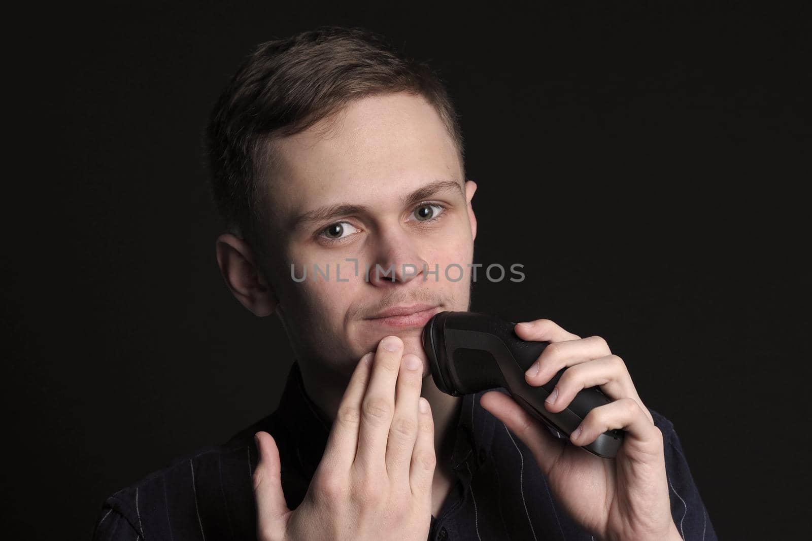 Shave safely. A young man shaves his face with an electric razor by Olga26